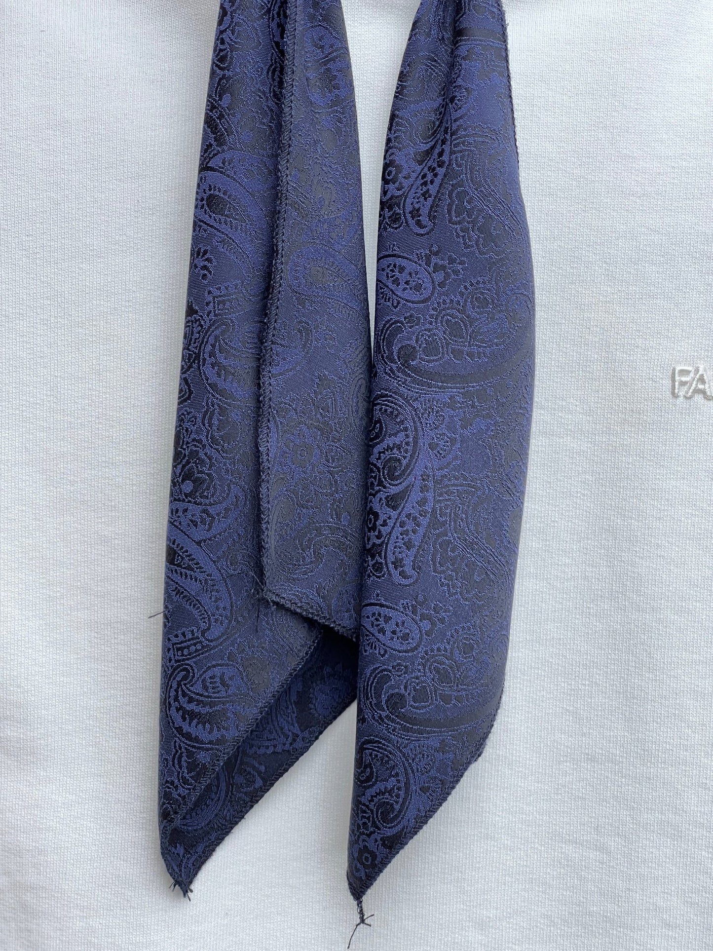A dark blue paisley tie made in Italy draped against a light fabric background.