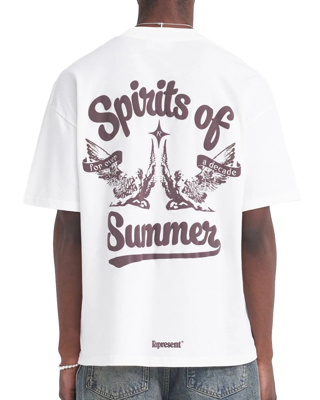 A person wearing a REPRESENT REPRESENT MLM410-72 SPIRITS OF SUMMER T-SHIRT WHI with the text "Spirits of Summer" in large font and "for over a decade" in smaller font, along with two illustrated birds. The REPRESENT MLM410-72 SPIRITS OF SUMMER T-SHIRT WHI has an oversized fit. Front of the shirt is not visible.