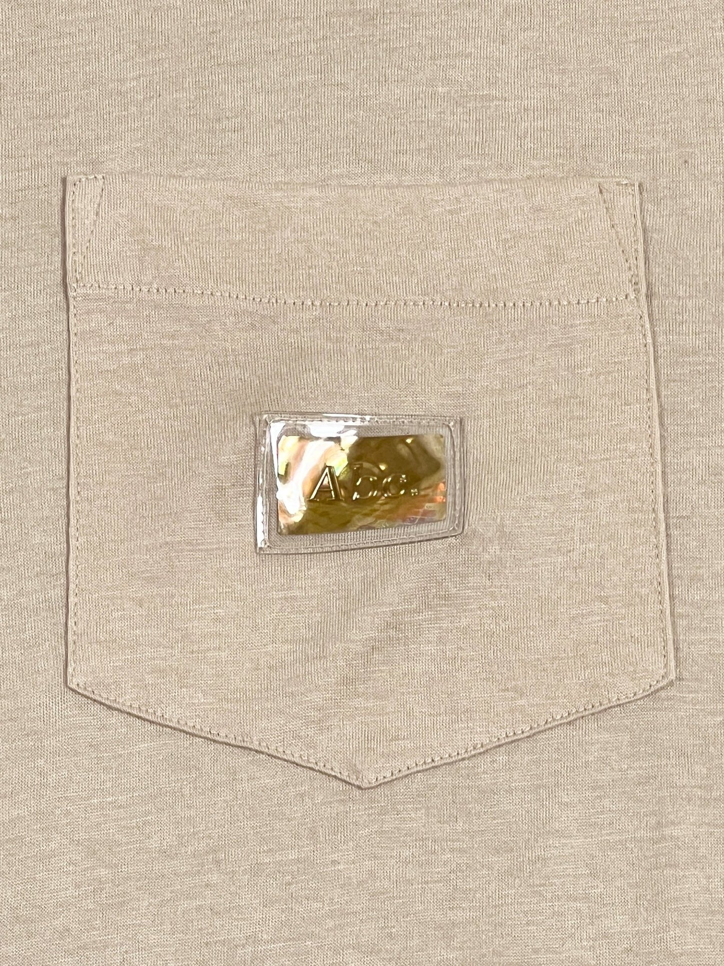 The pocket of a ADVISORY BOARD CRYSTALS S/S POCKET TEE FELDSPAR ECRU cotton t-shirt with a logo on it.