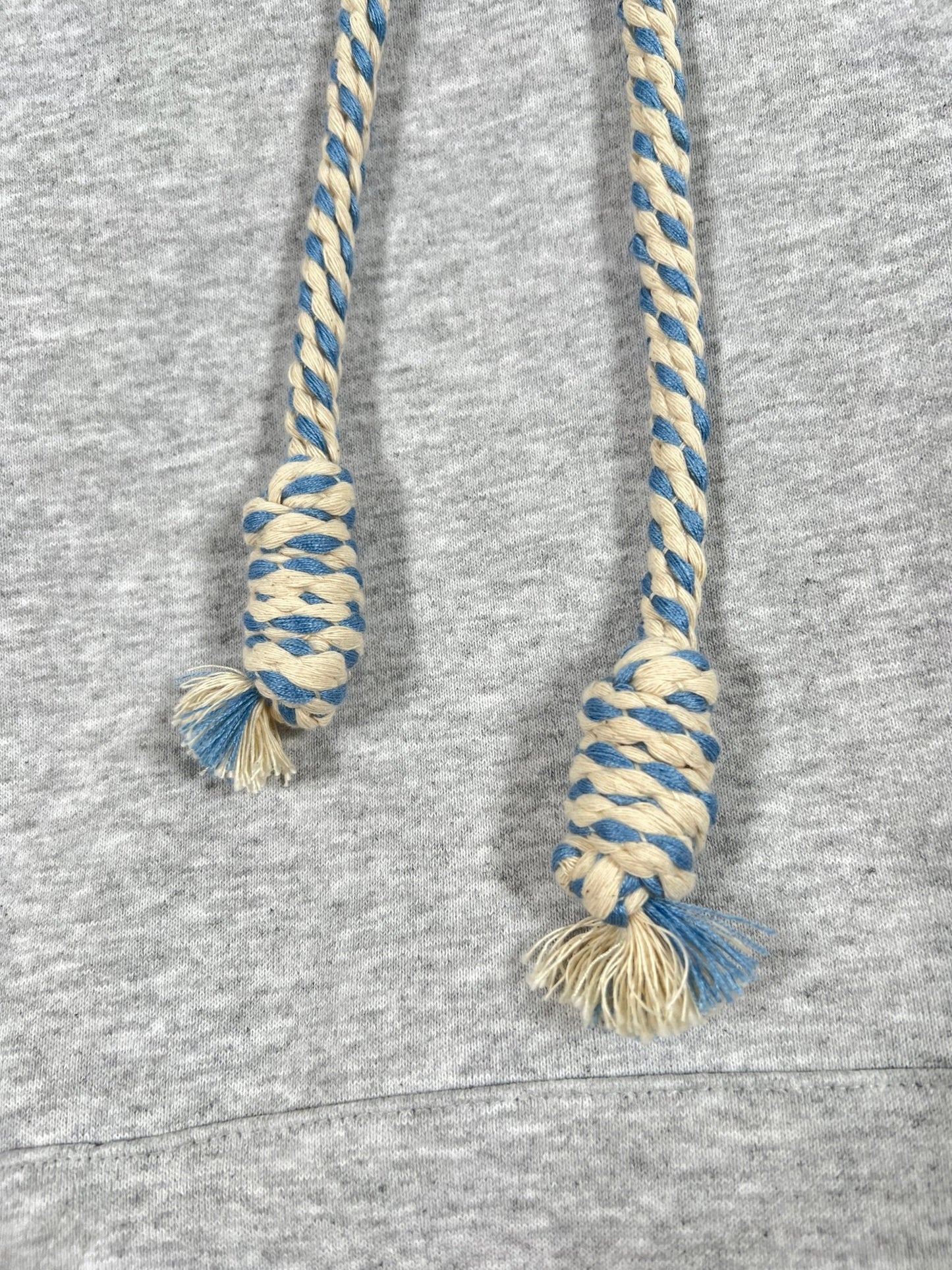 Close-up of blue and white braided drawstrings with thick rope texture lace detail on a grey AL AIN AHOX S150 YACHT LIMITED fabric background, likely part of a sweatshirt.