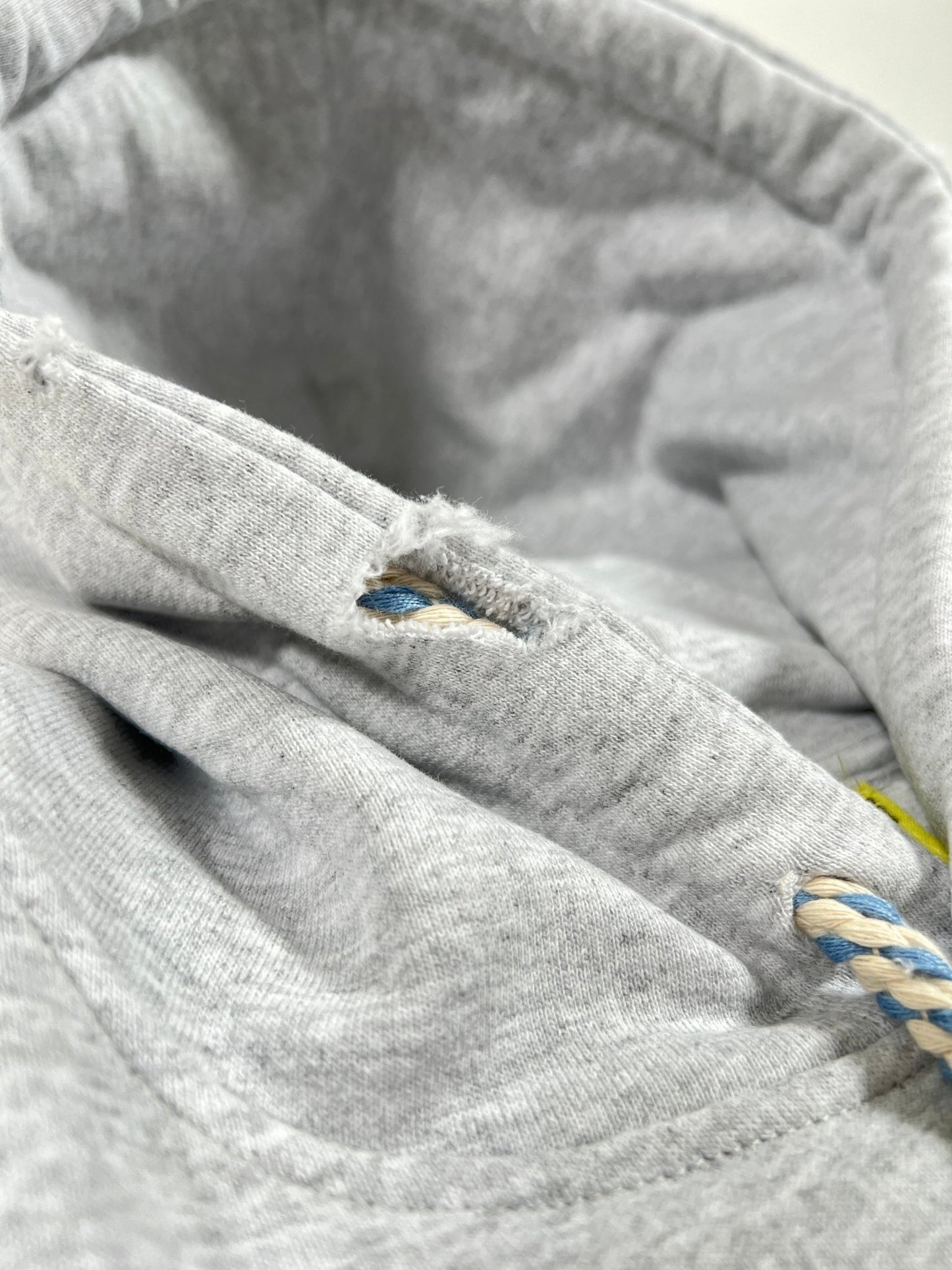 Close-up of a gray fabric with a small tear near a blue and white braided cord, reminiscent of the thick rope texture lace detail found on a grey AL AIN AHOX S150 YACHT LIMITED hoodie.