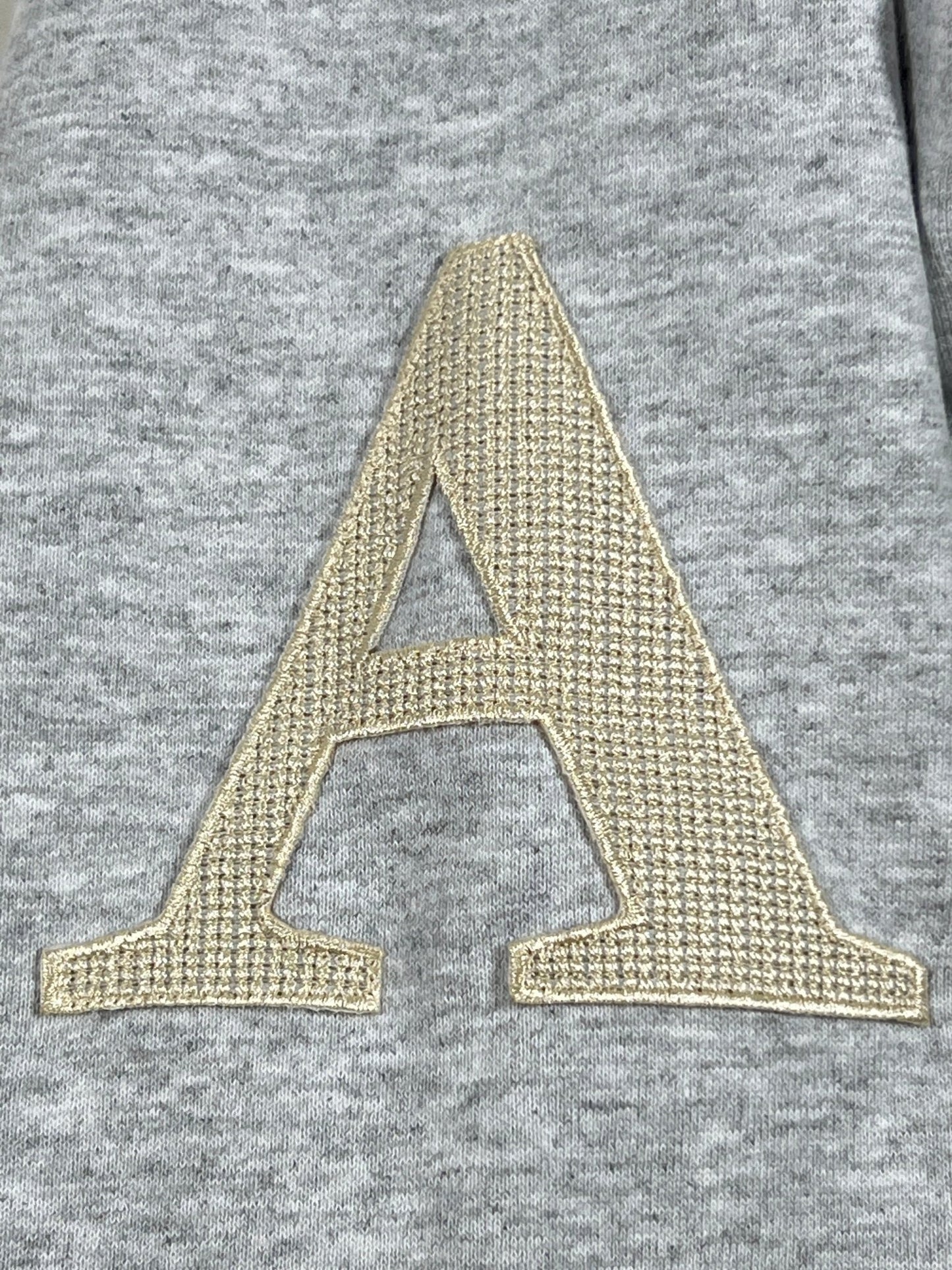 Close-up of a large, embroidered letter "A" in beige thread on a textured, grey AL AIN AHOX S150 YACHT LIMITED hoodie fabric background.
