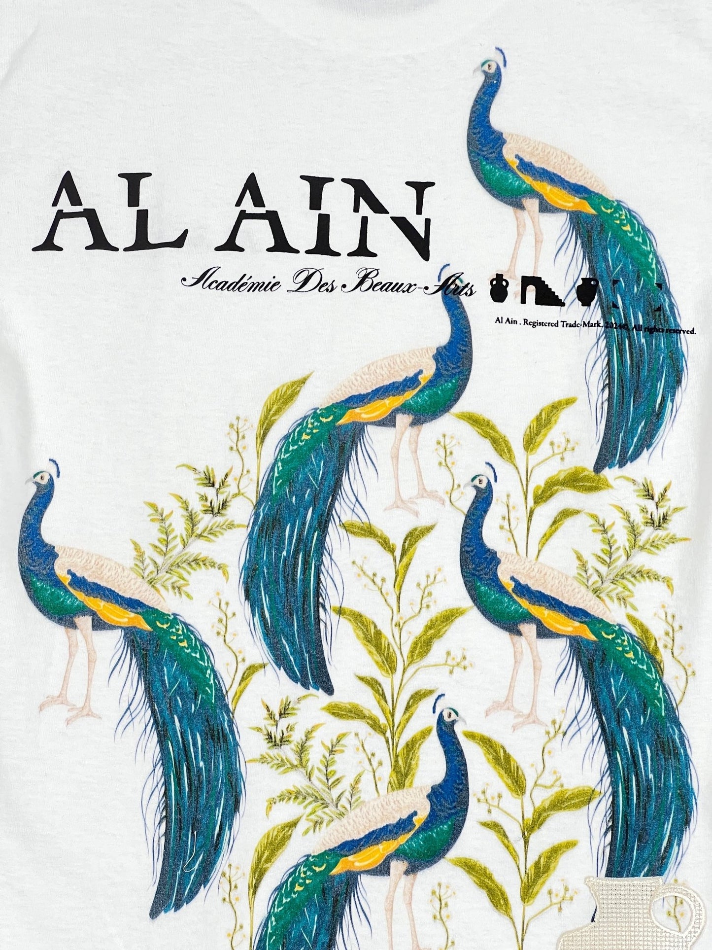 Illustration of four peacocks with vibrant blue and green feathers surrounded by green foliage, embroidered brand name "AL AIN AL AIN AMHX S121 PEACOCK BLANC" in stylized fonts, perfect for a graphic t-shirt.
