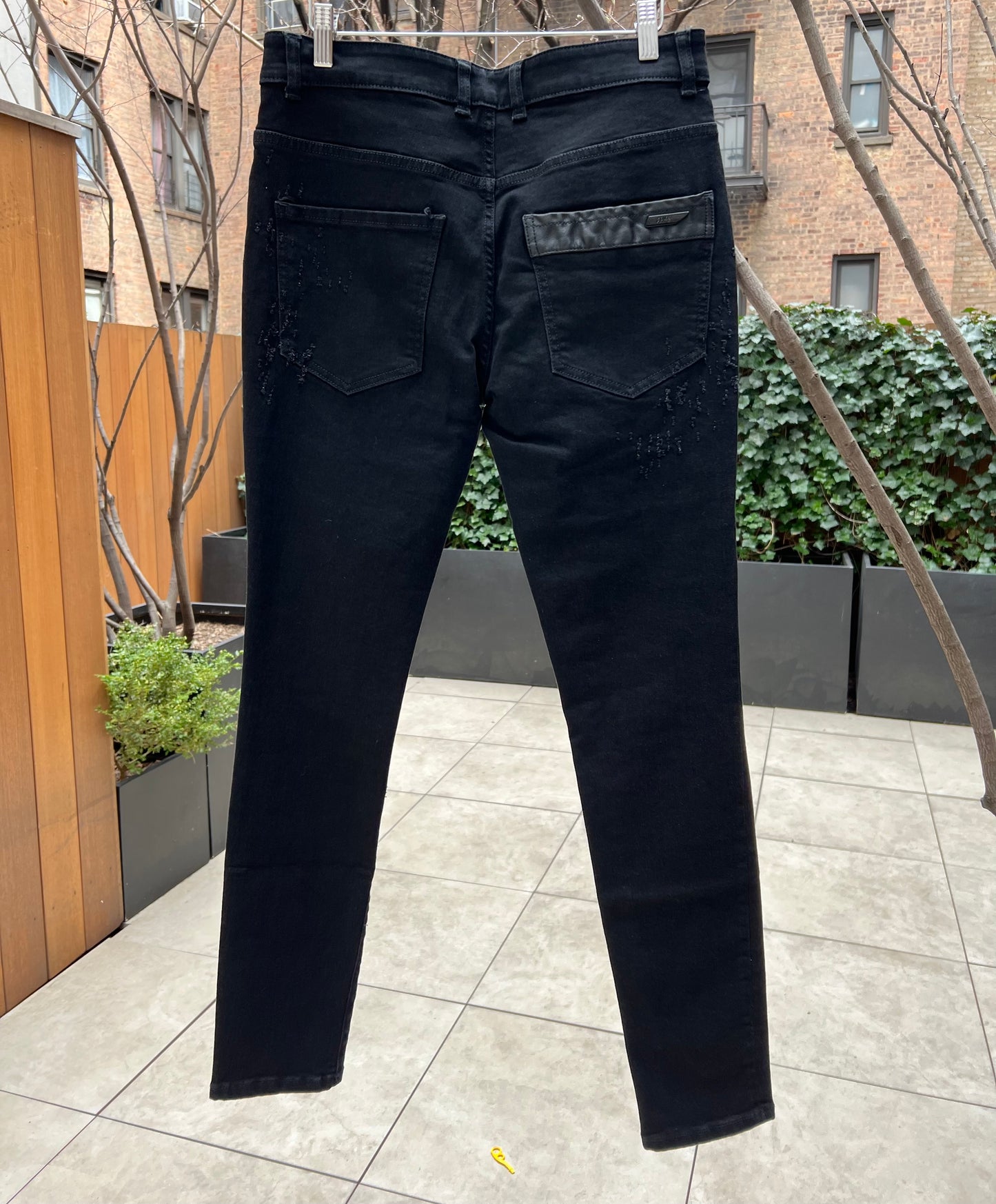 A pair of RH45 premium denim jeans hanging outdoors against a backdrop of trees and a building.