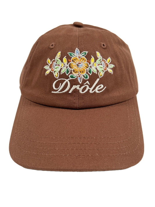 A DRÔLE DE MONSIEUR B-CP112 LA CASQUETTE DROLE FLEURIE BROWN hat with the word "DROLE DE MONSIEUR" embroidered on it.