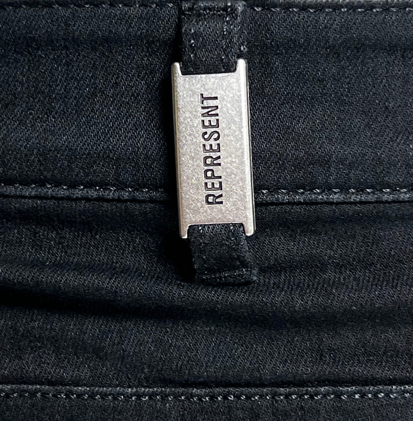 A close up of a pocket with a distressed-style label from streetwear brand REPRESENT M07044 DESTROYER DENIM BLACK on it.