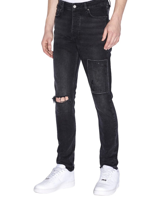 A man wearing black slim tapered Ksubi Chitch Flight Black jeans with holes on the knees.