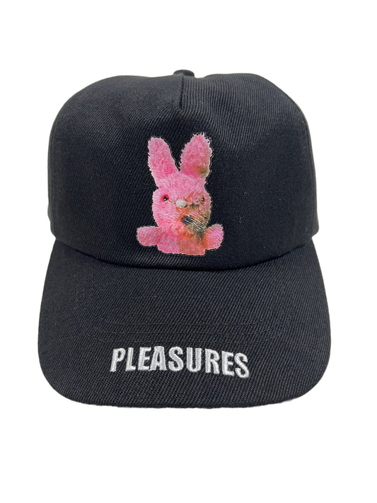 A black twill curved brim cap with a pink bunny on it that says PLEASURES BUNNY SNAPBACK BLACK by PLEASURES.