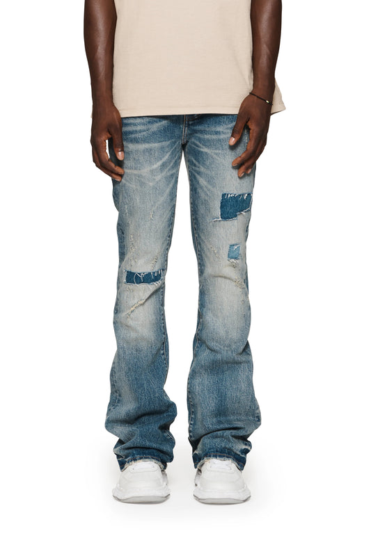 A man wearing a Purple Brand P004-PRFL Patch Repair Flare Mid Indigo jeans.