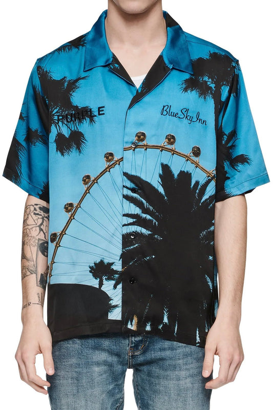 A man wearing a PURPLE BRAND P354-PBCD PURPLE X BLUE SKY SHIRT AOP with palm trees and a ferris wheel.