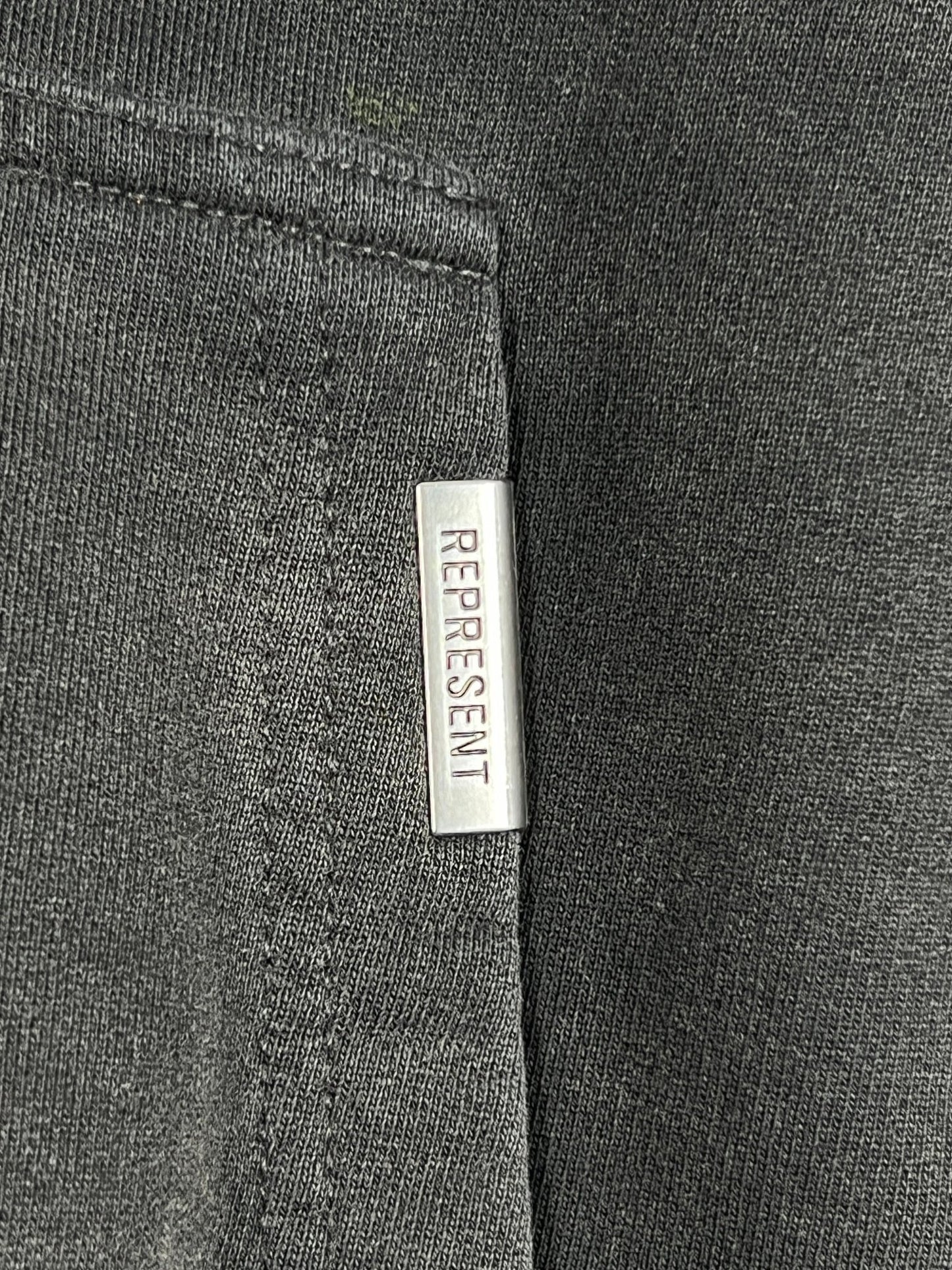 A close up of a grey graphic hoodie with a REPRESENT MLM435-444 REBORN HOODIE AGED label on it.