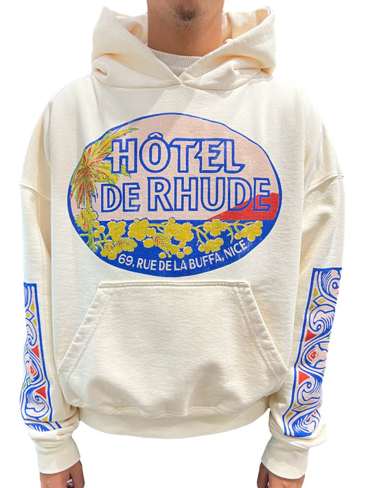 A man wearing a RHUDE HOTEL HOODIE VTG WHITE that says Hotel de Rhude.