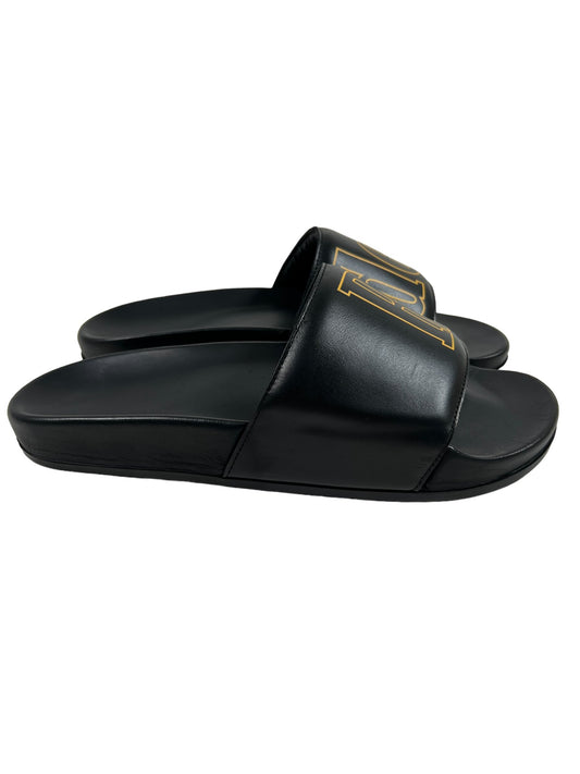 A pair of RHUDE black leather slide on sandals with a gold logo.