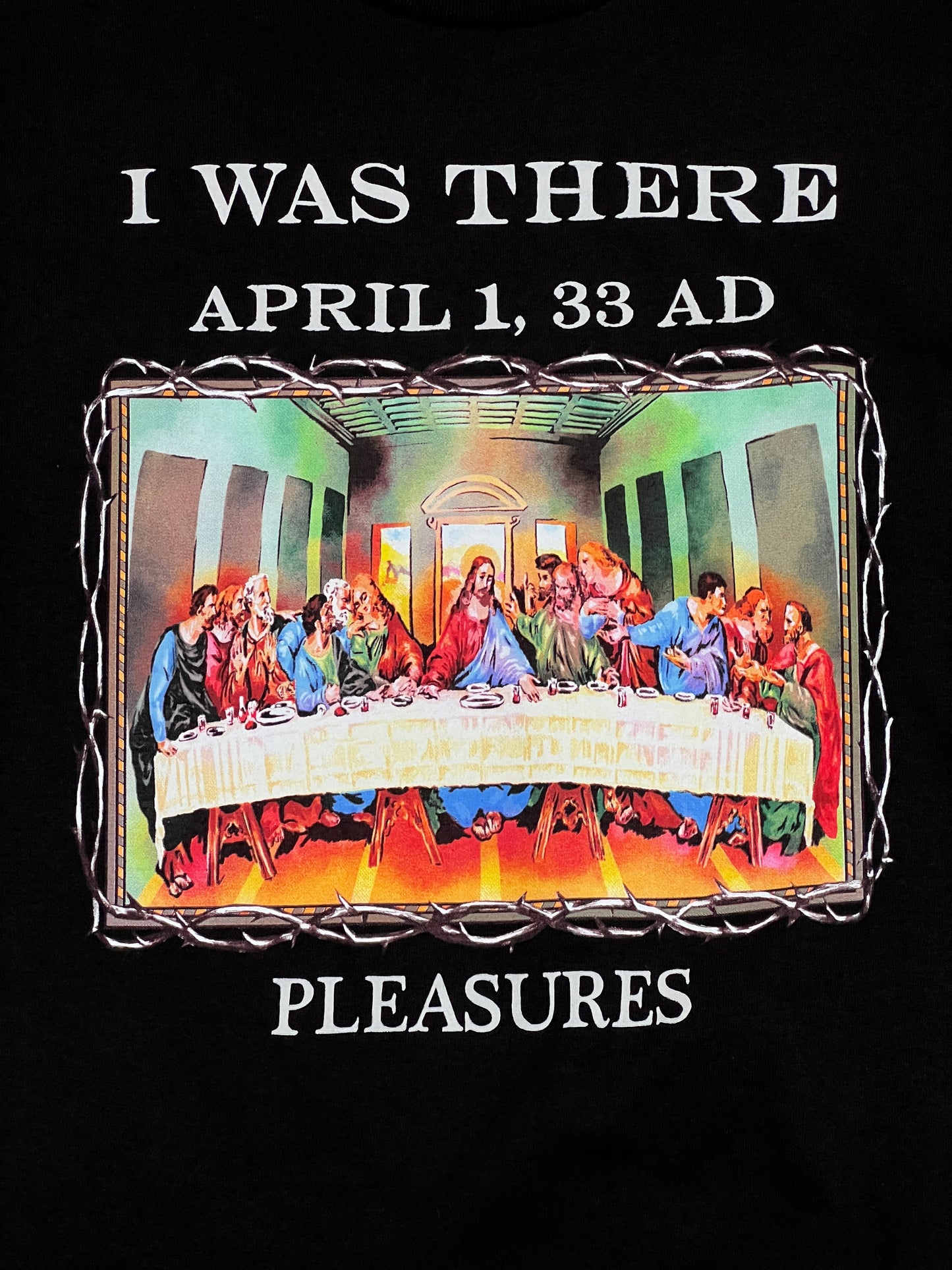 The Pleasures Supper T-Shirt in Black/Black by PLEASURES showcases "I WAS THERE APRIL 1, 33 AD PLEASURES" text around a Last Supper image and is crafted from 100% cotton for comfort and style.