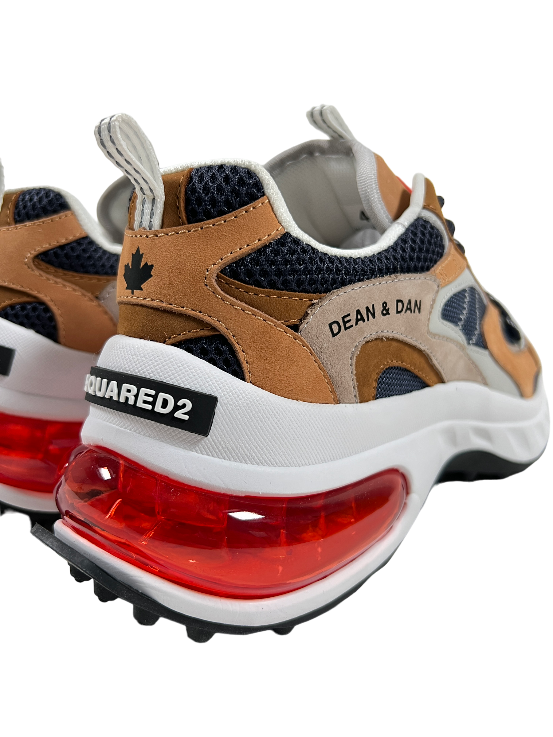 Close-up of beige, grey, and blue Dsquared2 SNM0307 sneakers featuring a mesh and nubuck leather texture with red air-cushioned rubber soles. The design includes a maple leaf motif and the "DEAN & DAN" text alongside "DSQUARED2" on the heel.