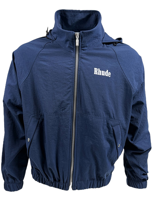 Navy blue nylon RHUDE PALM TRACK JACKET NAVY with "Rhude" written in white on the left chest. Featuring a high collar, elastic cuffs, and hem, along with two snap-button pockets on the front, this premium track jacket also showcases the RHUDE Crest design for added flair.