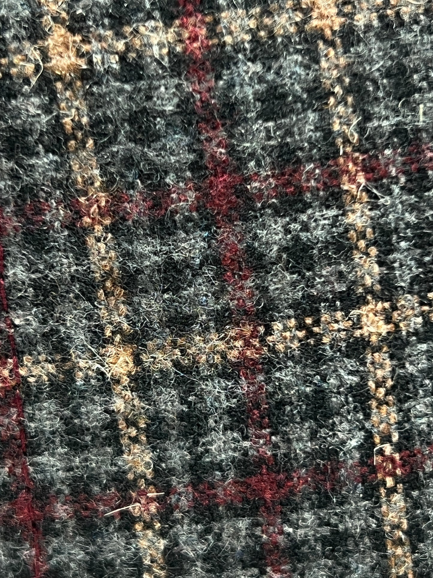 Close-up of the PLEASURES HAPPIER PLAID TRUCKER MAROON fabric, showcasing its textured plaid pattern in shades of grey, red, and beige, woven from polyester and nylon.