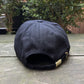 A black VERSACE E72GAZK10-EZG010-EG89 hat with an adjustable strap on a wooden surface.