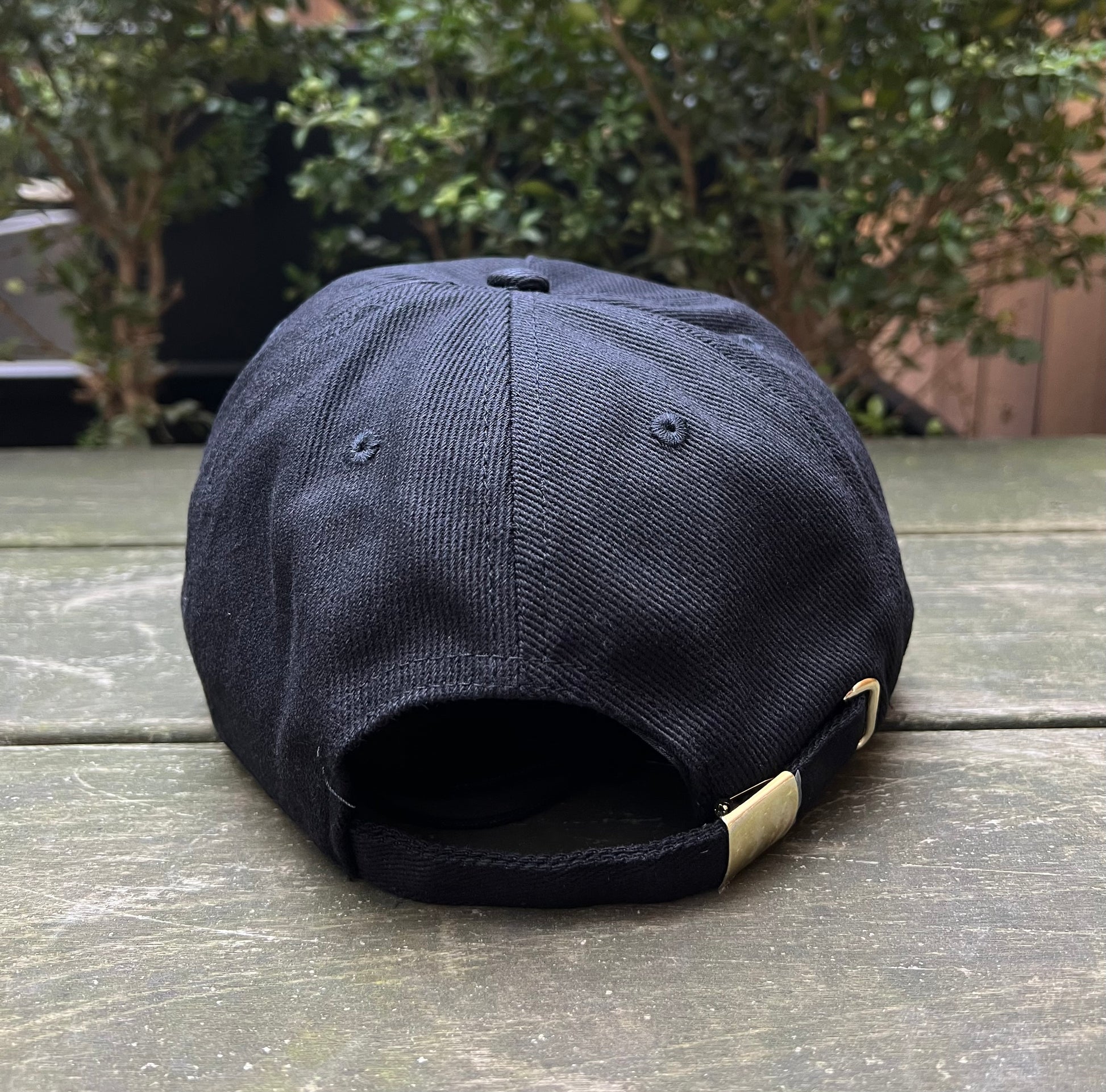 A black VERSACE E72GAZK10-EZG010-EG89 hat with an adjustable strap on a wooden surface.