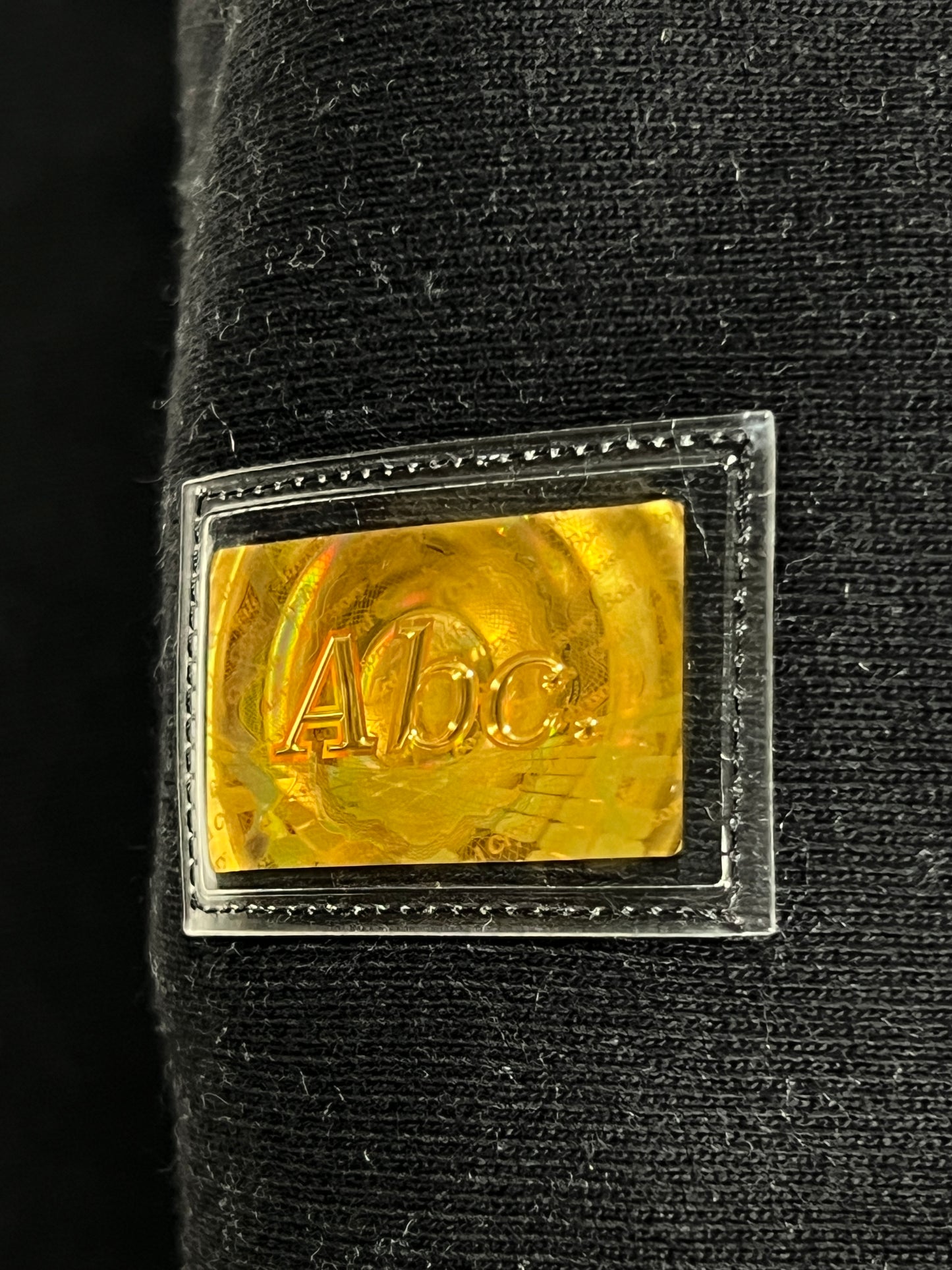 A close up of a gold label on ADVISORY BOARD CRYSTALS sweatpants in black polyester.