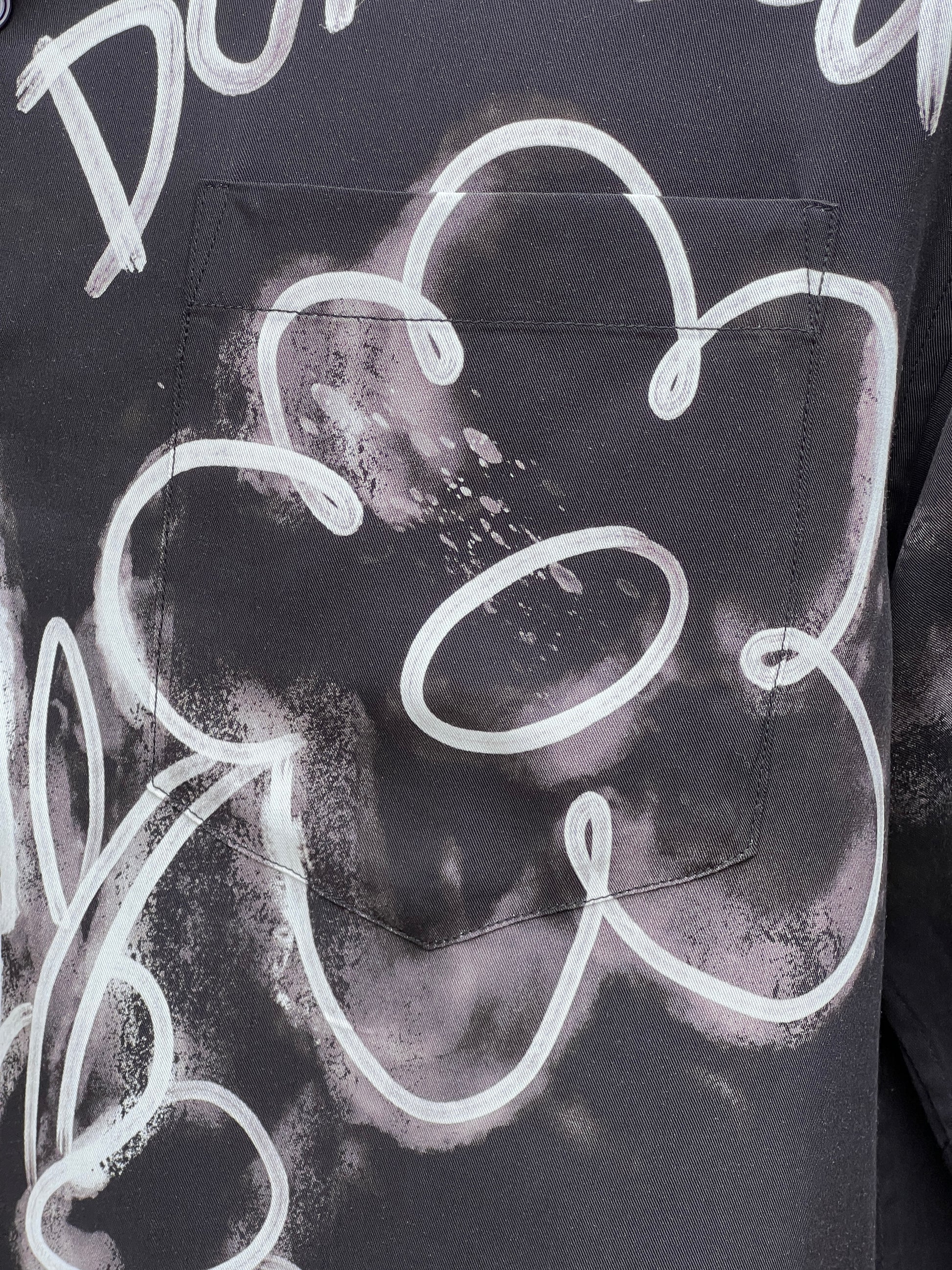 Close-up of a pocket on a dark fabric with a decorative white flower outline and abstract white patterns, featured on a DOM REBEL DOMREBEL CHAINED SHIRT BLACK crafted from a rayon Tencel blend.