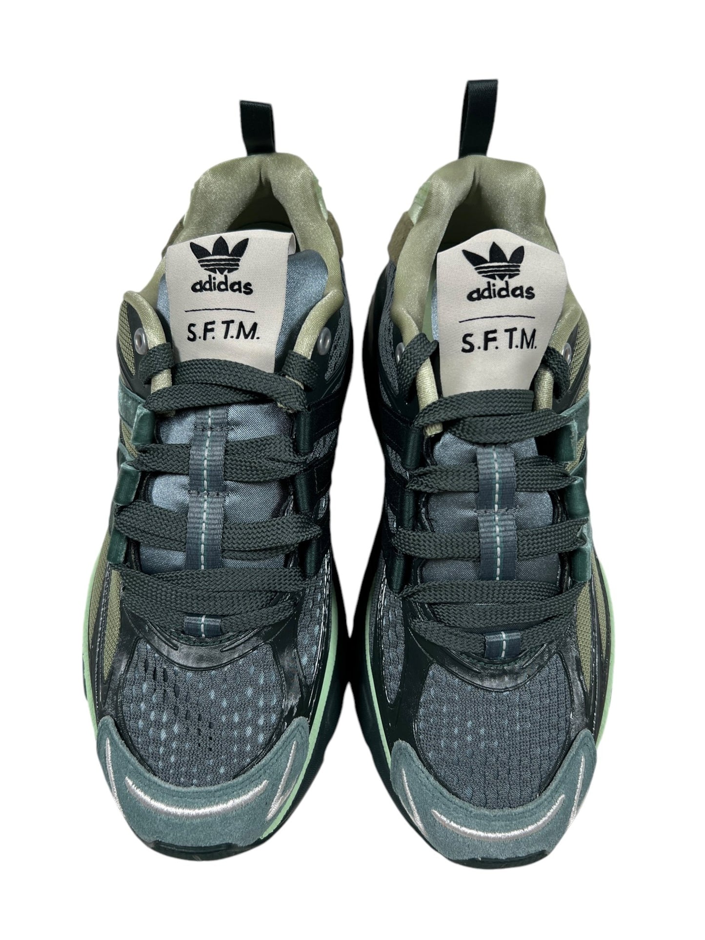 A pair of dark green Adidas X Song For The Mute Jh9008 Adistar Cushion Sft Shagr sneakers with "S.F.T.M." on the tongue, featuring a mesh and synthetic upper with a lace-up closure, offering comfort as your go-to trainers.