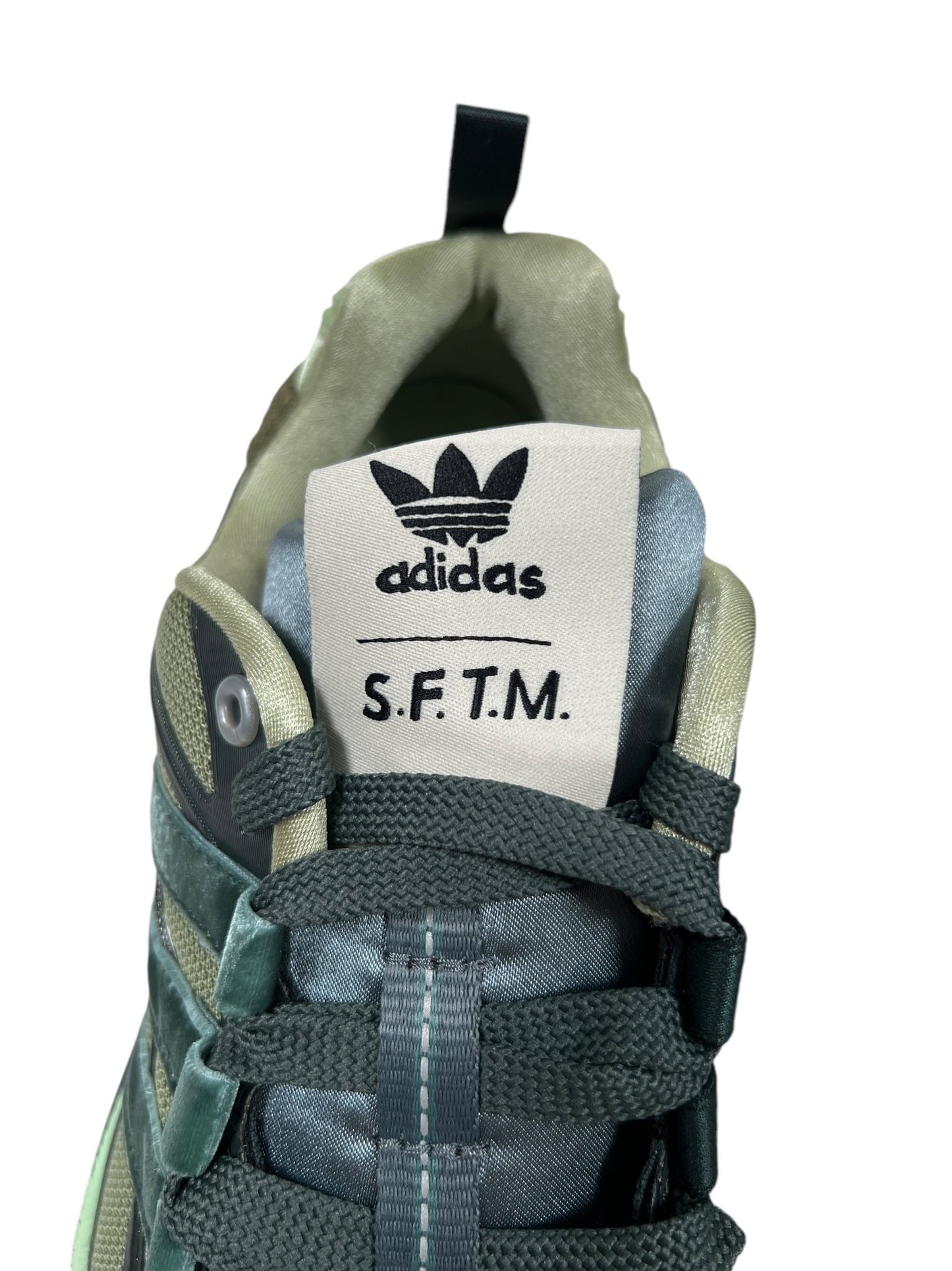 Close-up view of an Adidas sneaker featuring "S.F.T.M." on the tongue label, highlighting the Adistar Cushion design for comfortable trainers by ADIDAS x SONG FOR THE MUTE.