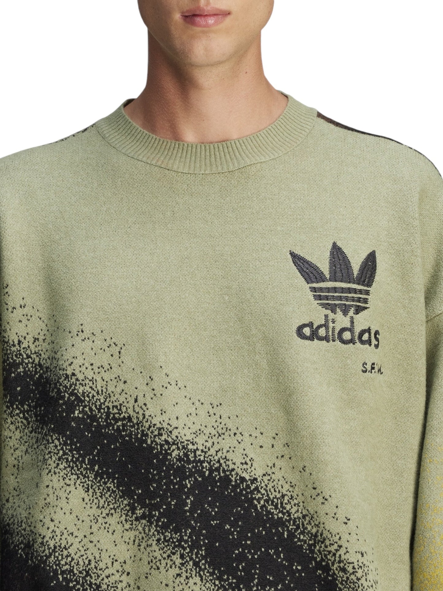 Close-up of an individual wearing the Adidas X Song For The Mute Ji9643 Adi004 Knitswea Tengr, showcasing a black speckled design and the iconic Adidas logo on the chest.