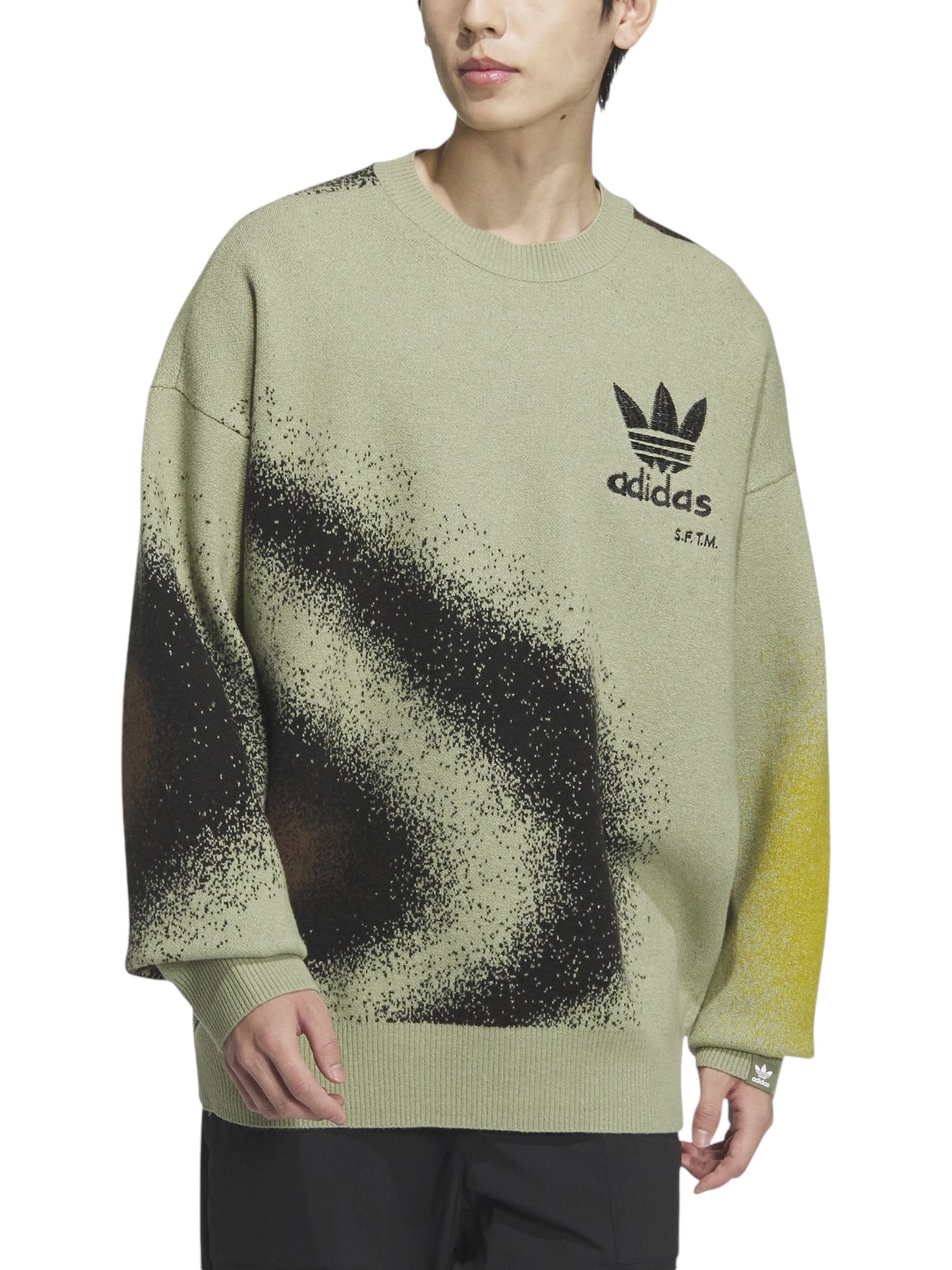 The individual wears the Adidas X Song For The Mute Ji9643 Adi004 Knitswea Tengr, an oversized green sweater adorned with black and yellow abstract patterns and highlighted by the iconic Adidas logo on the chest—an eye-catching piece from the ADIDAS x SONG FOR THE MUTE collaboration collection.