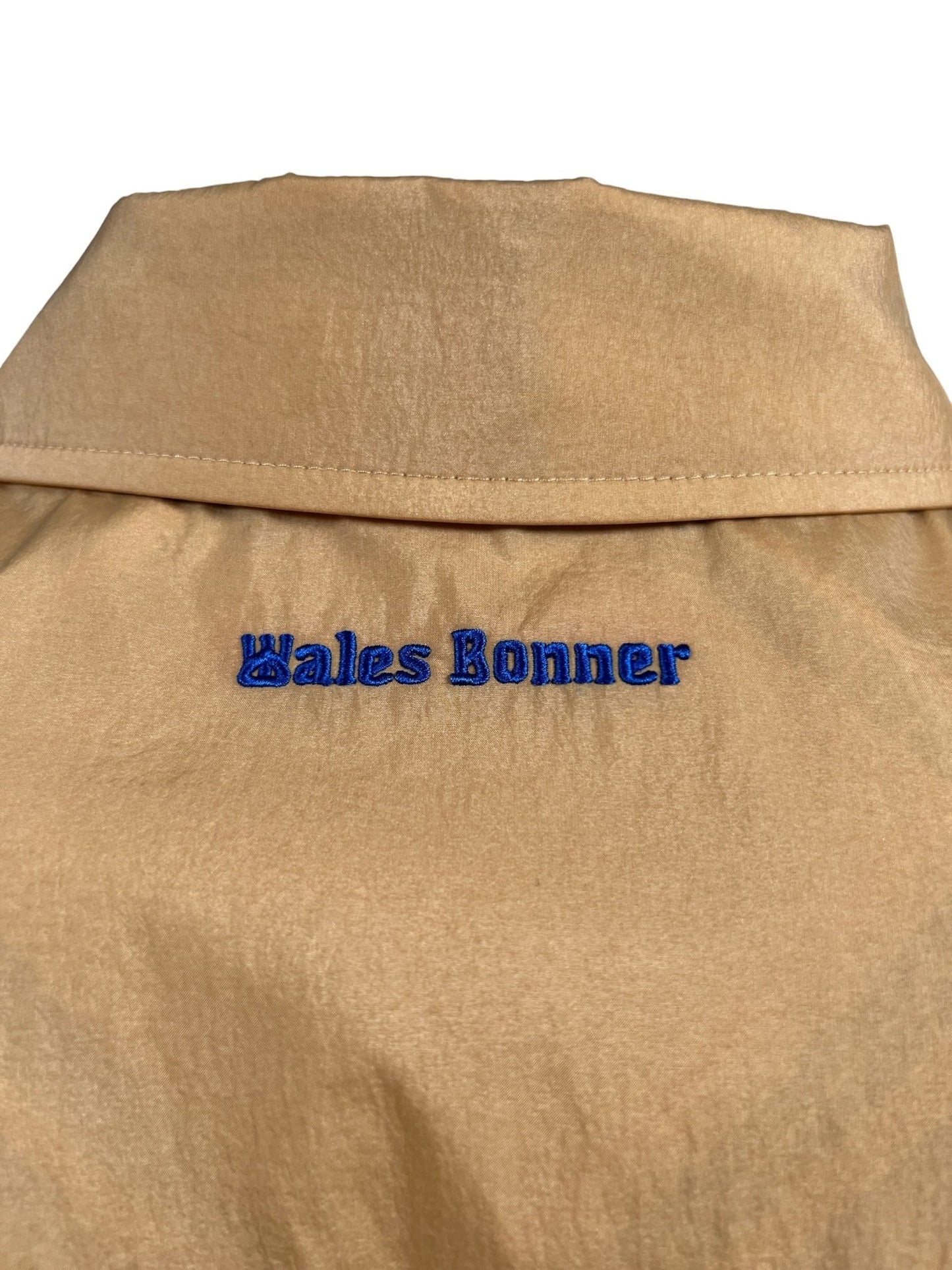 Beige fabric with the "ADIDAS X WALES BONNER IW3601 WB RVRSBL HARRI BEIGWB" embroidered in blue thread at the neckline.