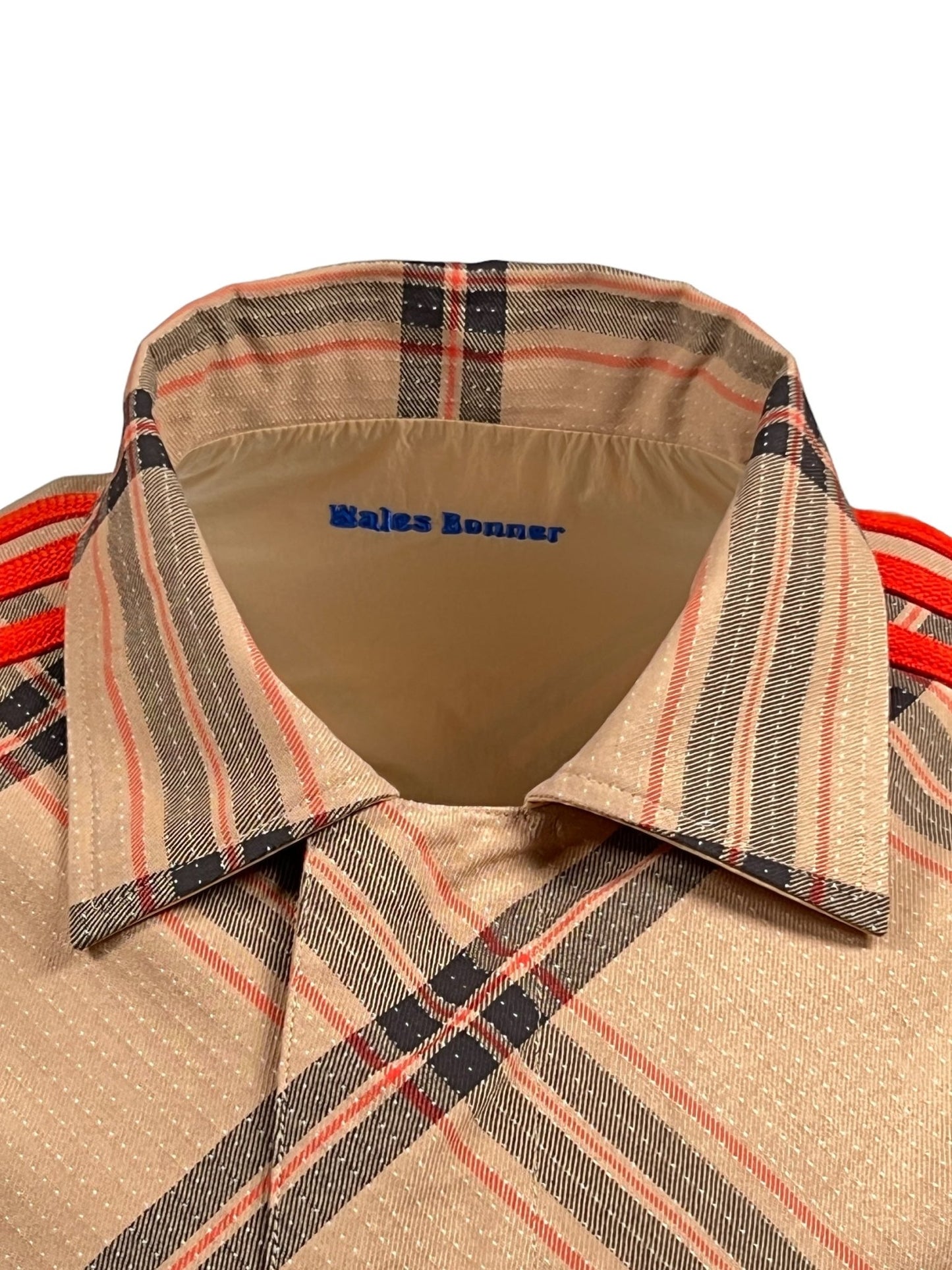 Close-up of the collar and tag of a beige ADIDAS X WALES BONNER IW3601 WB RVRSBL HARRI BEIGWB shirt with a classic plaid design and the logo print "Wales Bonner" inside.