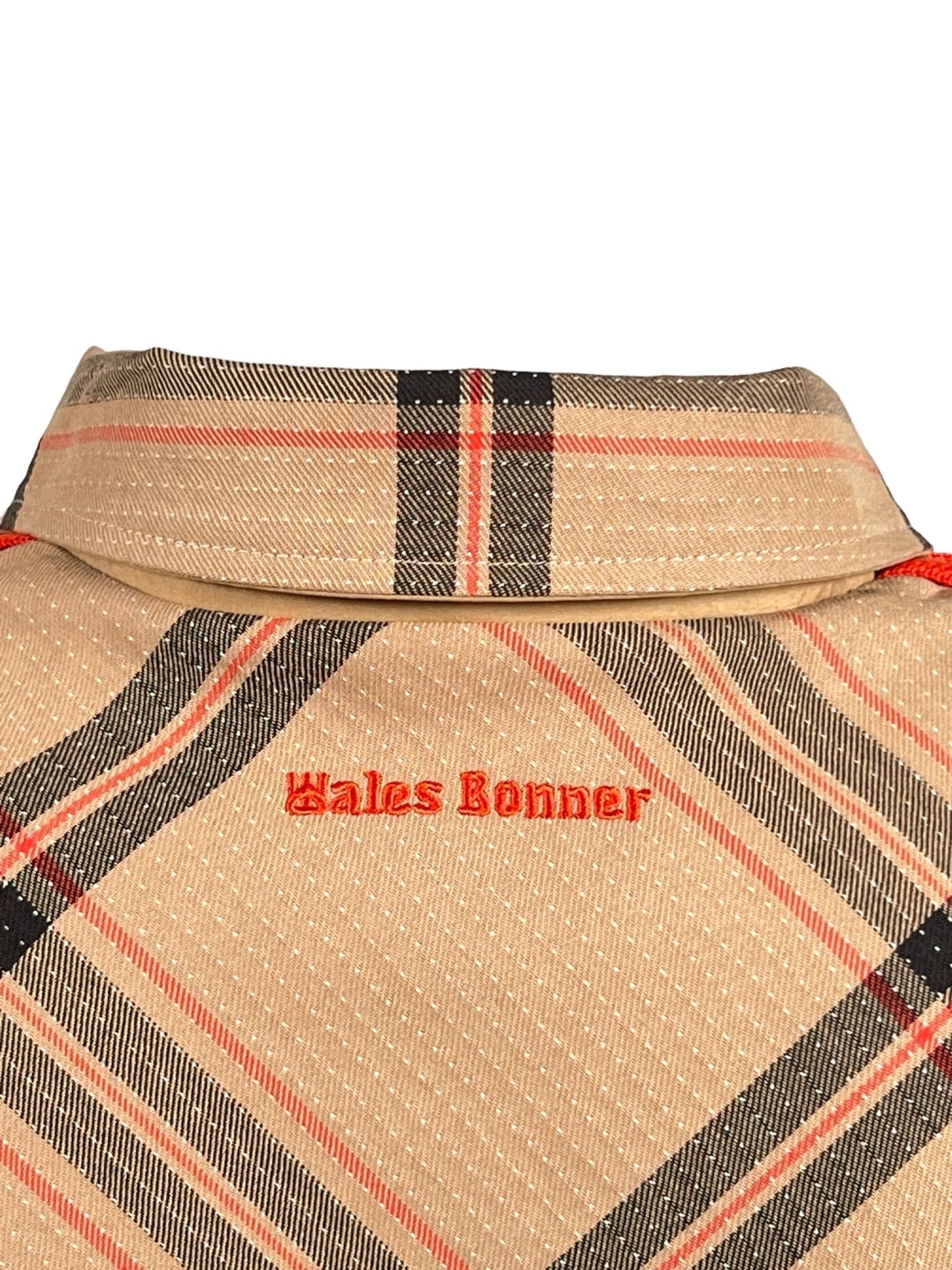 Close-up of a beige ADIDAS x WALES BONNER IW3601 WB RVRSBL HARRI BEIGWB reversible jacket with a red and black plaid pattern and "Wales Bonner" embroidered in red on the chest.