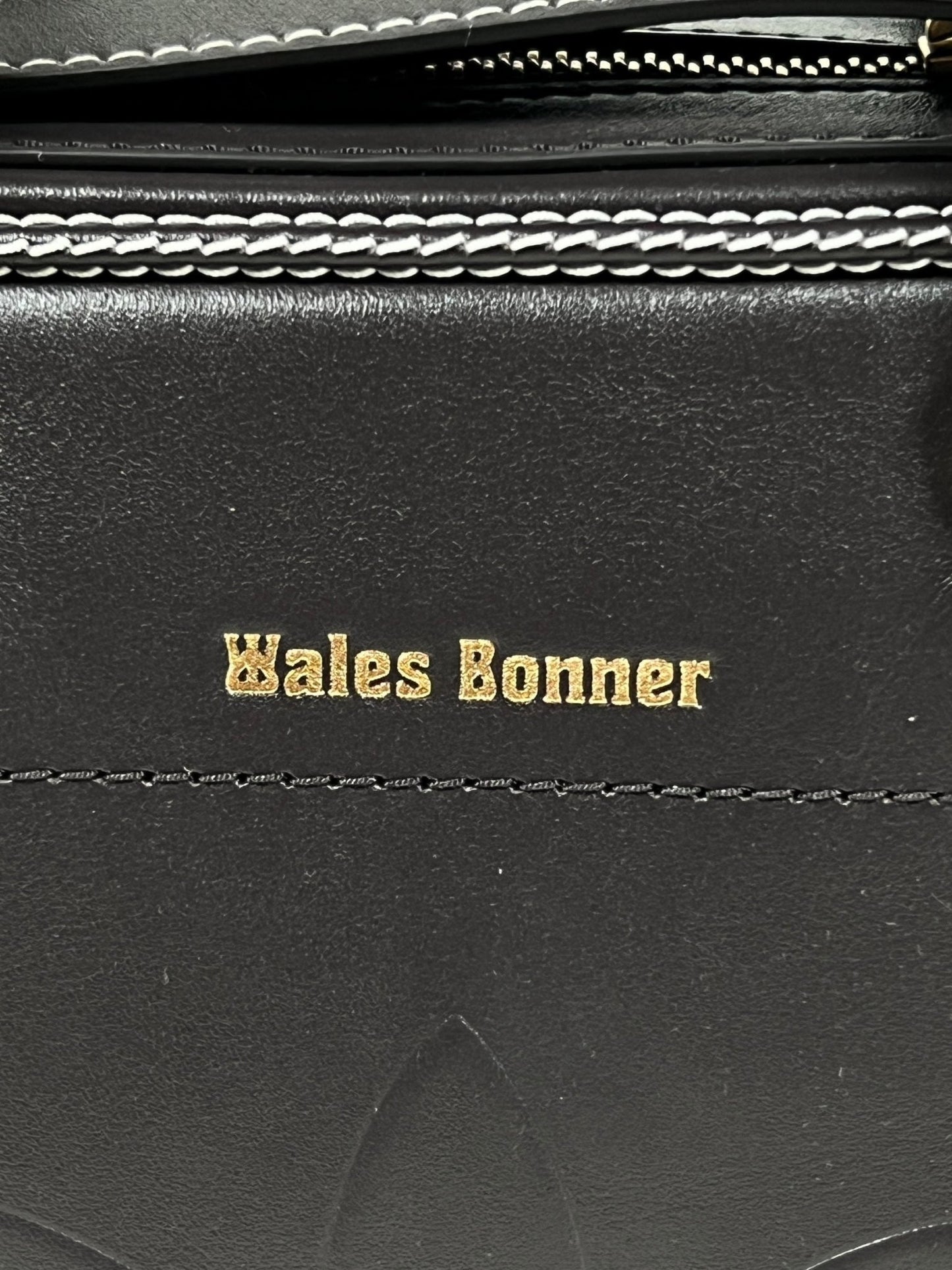 Close-up of a black leather item with "ADIDAS x WALES BONNER" embossed in gold lettering, featuring a visible zipper with silver teeth above, part of the exclusive Adidas IW3600 Wb Rvrsbl Mac Beigwb collaboration.