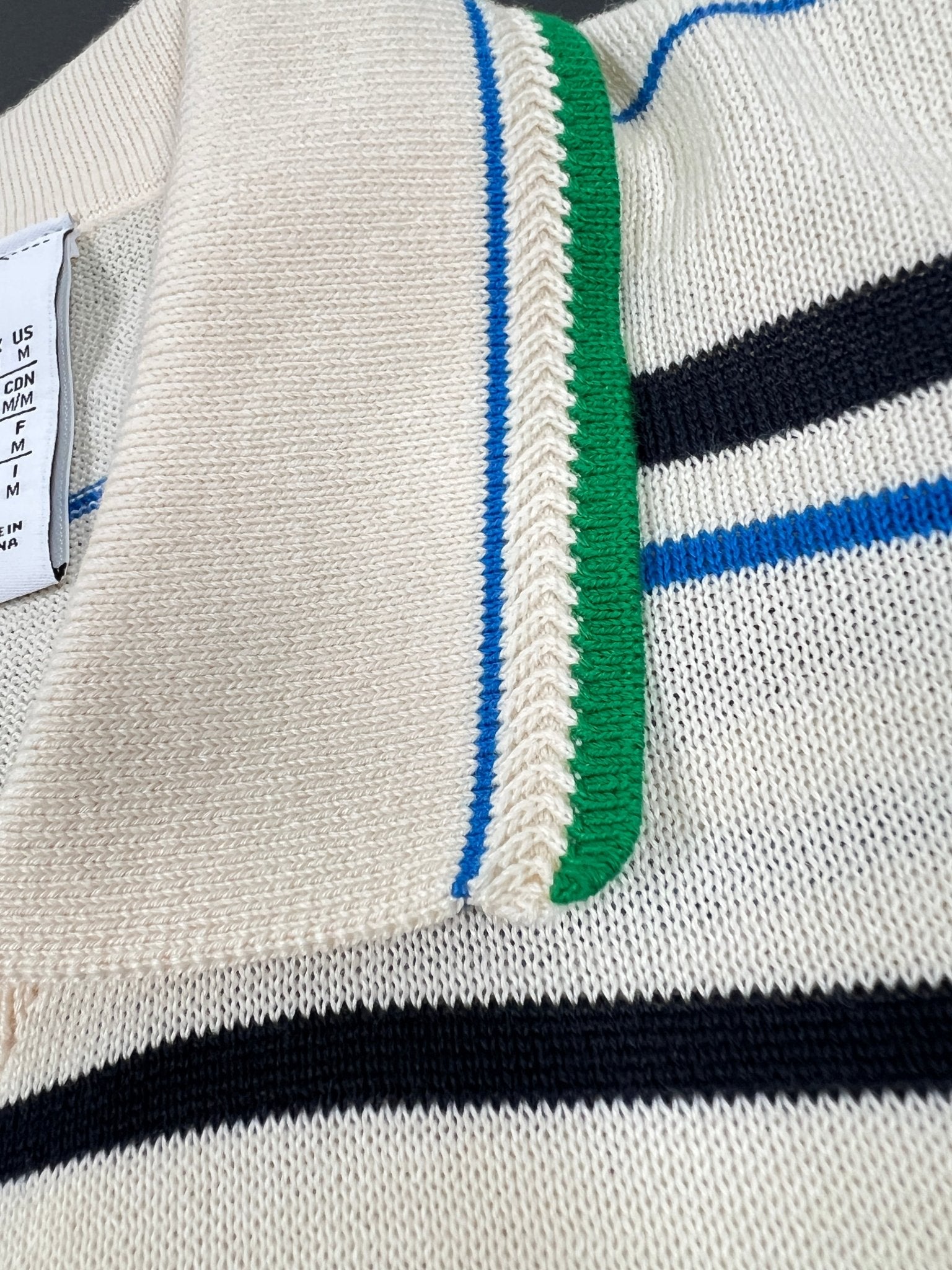 Close-up of the Adidas x Wales Bonner JM8203 WB Knit Polo WonWh, a cream-colored polo with blue and black stripes, green and blue-edged collar, vintage-inspired design, and visible tag.