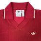 The Adidas x Wales Bonner JW1122 WB Terry Polo Cburg is a red collared sweater featuring white trim and an embroidered Trefoil logo, combining sporty elegance with retro style.