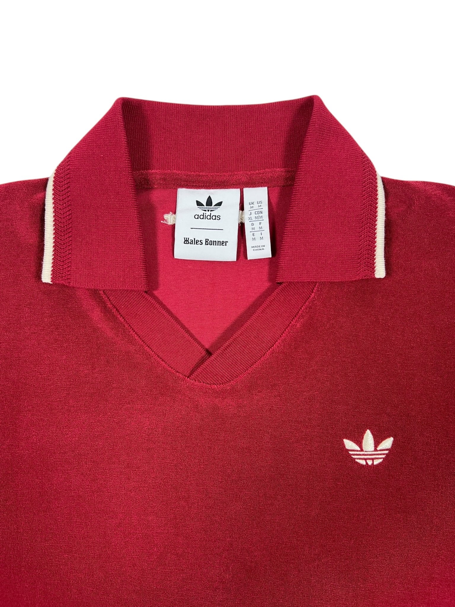 The Adidas x Wales Bonner JW1122 WB Terry Polo Cburg is a red collared sweater featuring white trim and an embroidered Trefoil logo, combining sporty elegance with retro style.