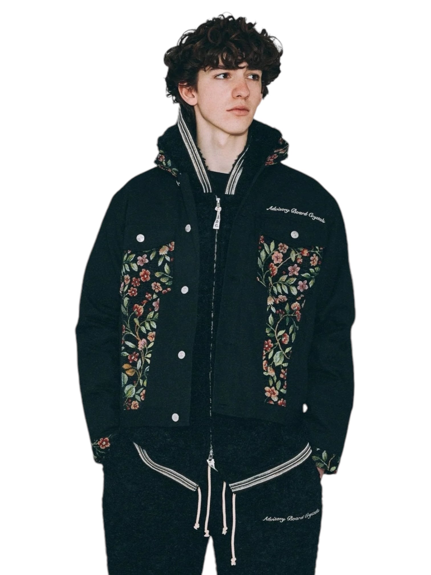 A person wearing the Advisory Board Crystals Abc. Floral Jacquard & Canvas Jacket in black from ADVISORY BOARD CRYSTALS, paired with matching pants, is looking to the side.