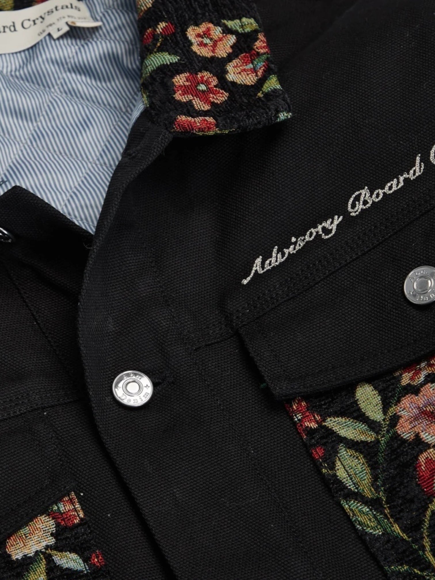 The Advisory Board Crystals Abc. Floral Jacquard & Canvas Jacket in black by ADVISORY BOARD CRYSTALS features floral embroidery on the collar and pockets, adorned with silver buttons and "Advisory Board" text on the chest. It is equipped with a quilted signature lining for enhanced comfort, making it a stylish and cozy choice.