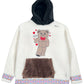 The Advisory Board Crystals Bear Patch Boa Fleece Hoodie in ecru from ADVISORY BOARD CRYSTALS features a black hood, a bear patch design with hearts, a brown pocket, and a colorful patterned trim at the bottom.
