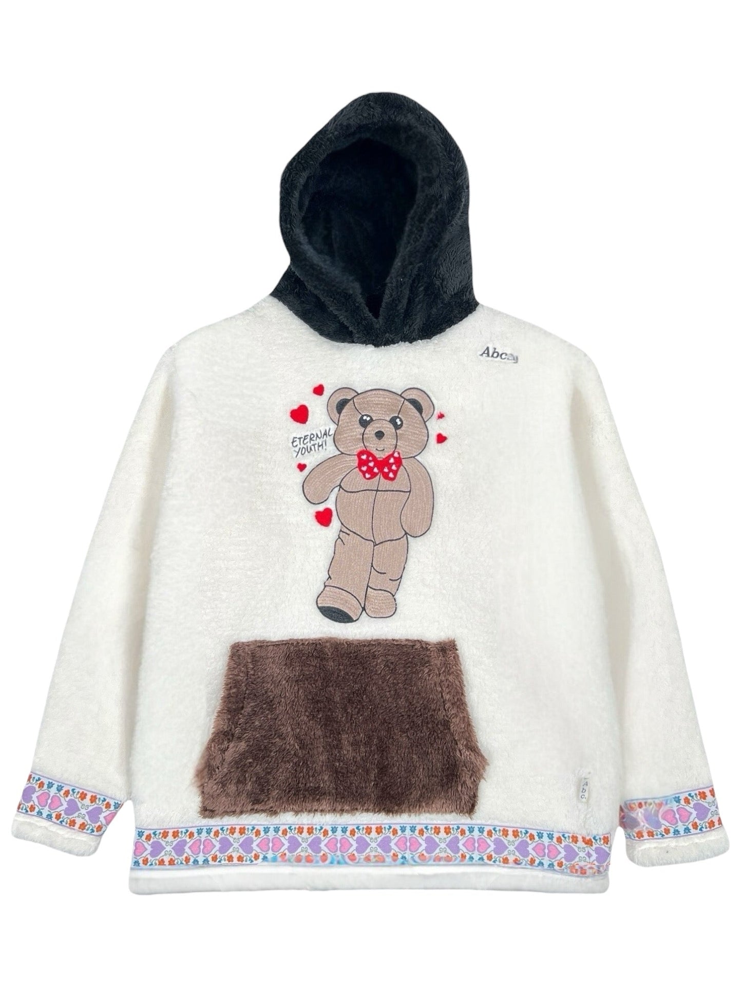 The Advisory Board Crystals Bear Patch Boa Fleece Hoodie in ecru from ADVISORY BOARD CRYSTALS features a black hood, a bear patch design with hearts, a brown pocket, and a colorful patterned trim at the bottom.