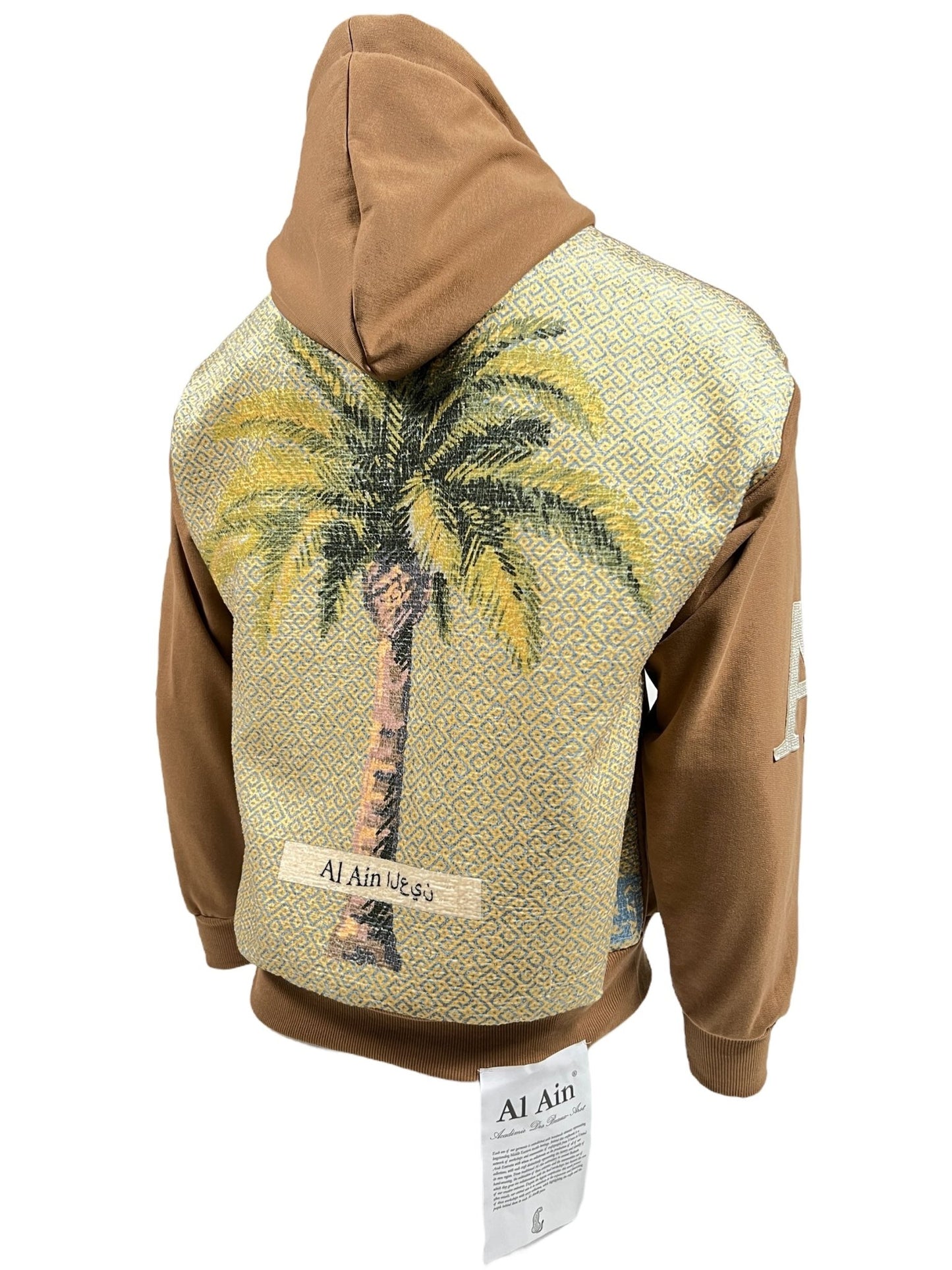 A brown hoodie featuring a large palm tree design and Arabic text on the graphic back. A tag with text hangs from the bottom, perfect for streetwear enthusiasts. Introducing the AL AIN AHOX S102 PALMIER CHAMEAU by AL AIN.
