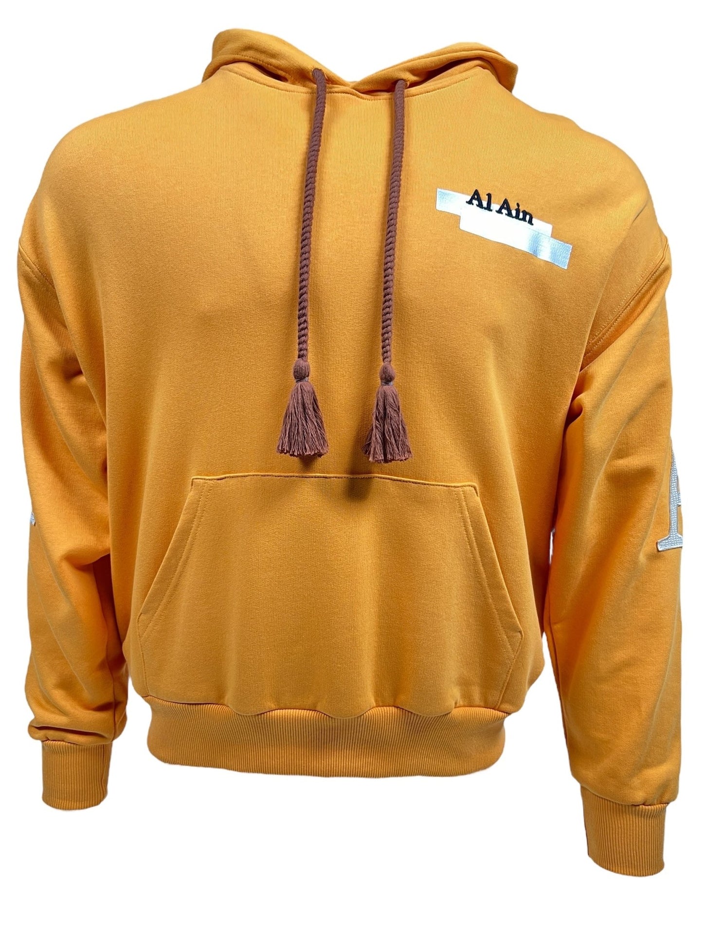 The Al Ain AHOX S108 Pouvoir Ocre hoodie by AL AIN features "Al Ain" text on the chest and is crafted from 100% cotton for ultimate comfort. It includes brown drawstrings and a front pocket, making it a perfect streetwear staple.