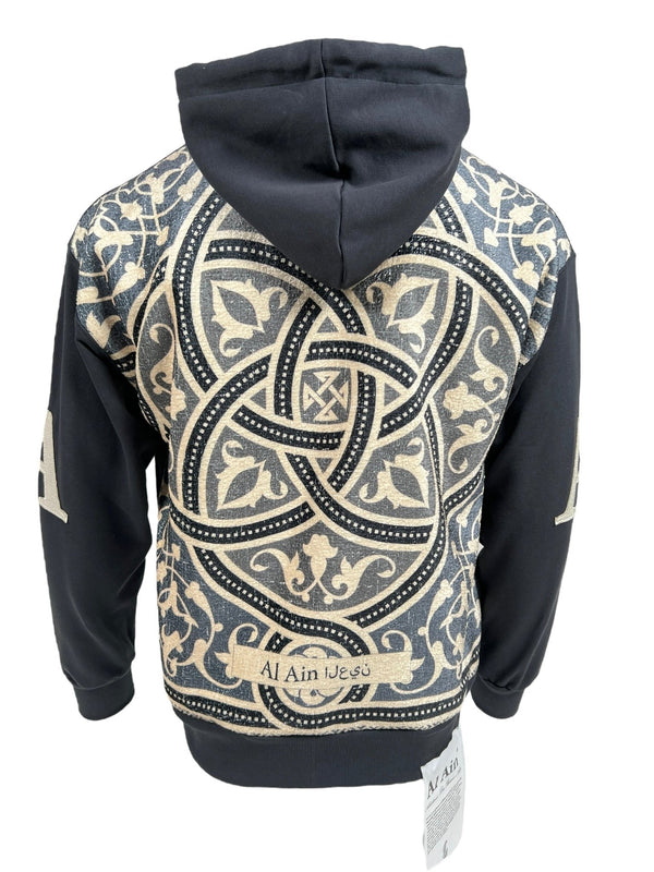 Rear view of a black AL AIN AHZX S103 SECRET NOIR hoodie with intricate beige geometric and floral patterns, crafted from 100% Cotton, and text "al ain jeu" visible.