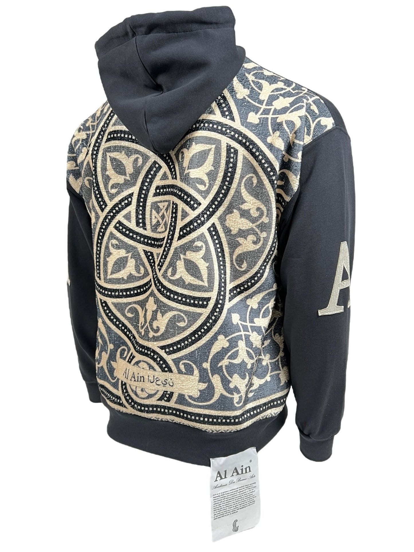 Rear view of a 100% cotton, hooded sweatshirt with intricate beige and black patterns and the text "AHZX S103 SECRET NOIR" on the sleeves, displayed on a mannequin.