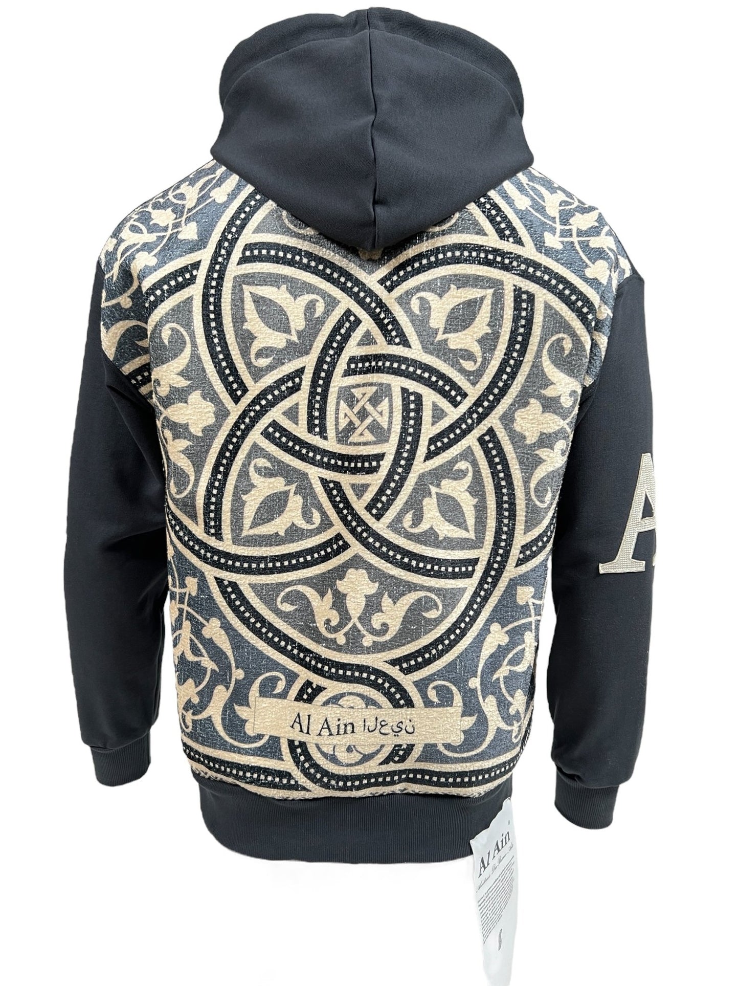 A black hooded streetwear sweatshirt with an intricate beige and grey geometric and floral pattern on the back, and "Al Ain 1968" written in Arabic and English at the bottom. This AL AIN AHZX S103 SECRET NOIR hoodie is crafted from 100% cotton for ultimate comfort.