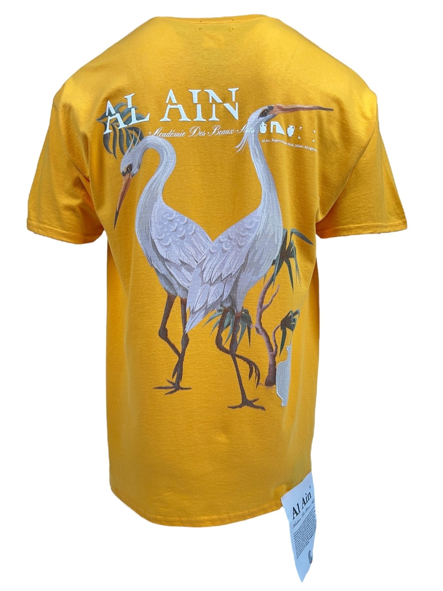 Introducing the Al Ain AMHX S120 Jabalia Ocre by AL AIN, a yellow graphic t-shirt adorned with illustrations of two cranes and palm trees, complete with the text "Al Ain" and additional small decorative elements. Crafted from 100% cotton, it offers ultimate comfort and durability.