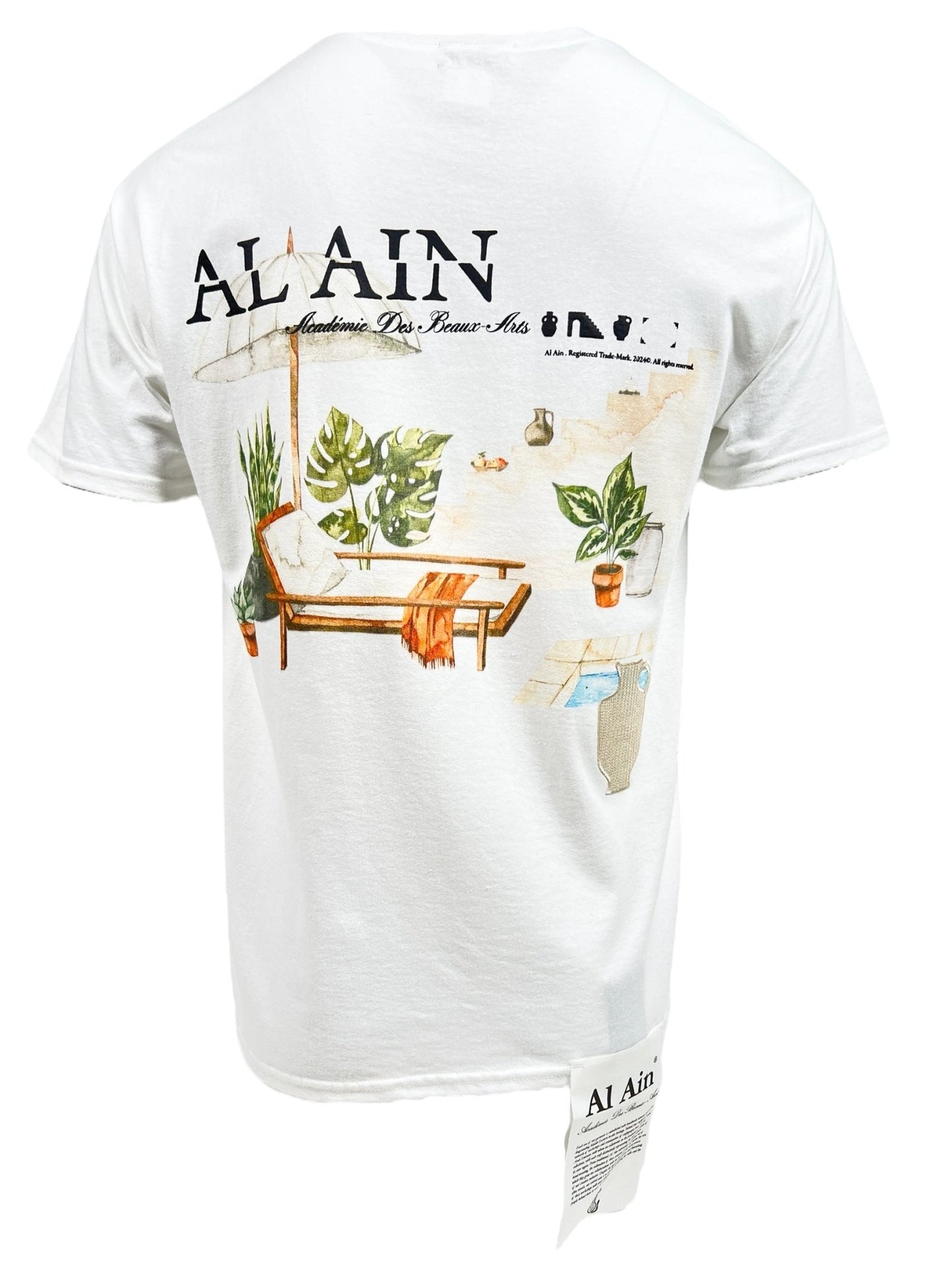 This Al Ain AMHX S124 Chill Blanc T-shirt, made from 100% cotton in white, showcases the "AL AIN" brand text and is enhanced with an embroidered depiction of a lounge chair, potted plants, and scattered leaves on the back.