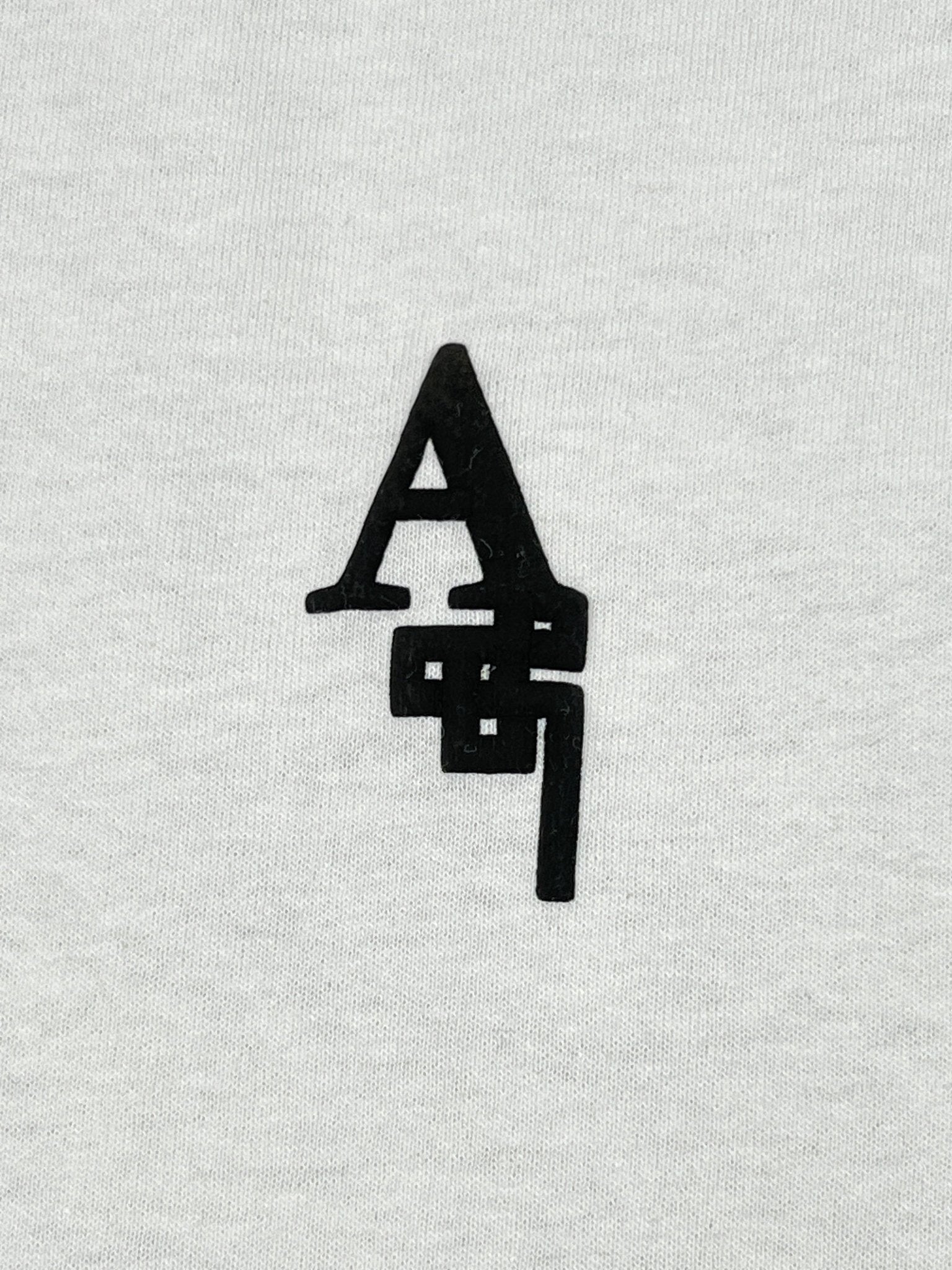 The Al Ain AMHX-S817 Sekaya T-shirt White by AL AIN features black stylized "A" and "g" letters overlapping vertically on a light gray, 100% cotton tee made in Italy.