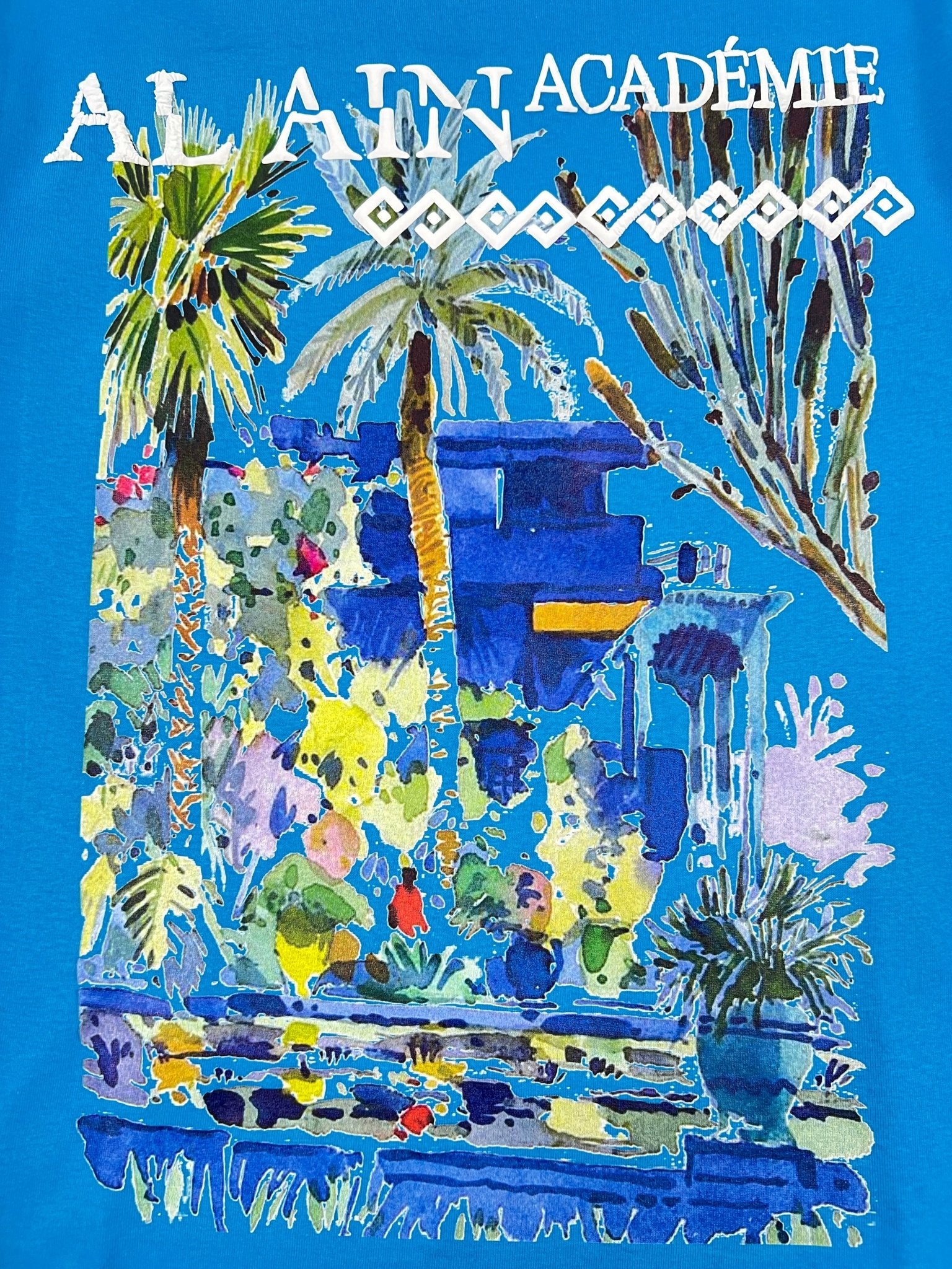 The Al Ain AMHX-S818 Majorelle T-shirt Orient by AL AIN features colorful palm trees, plants, and a blue building with "ALAIN ACADÉMIE" in white. Made of 100% cotton and proudly Made in Italy.