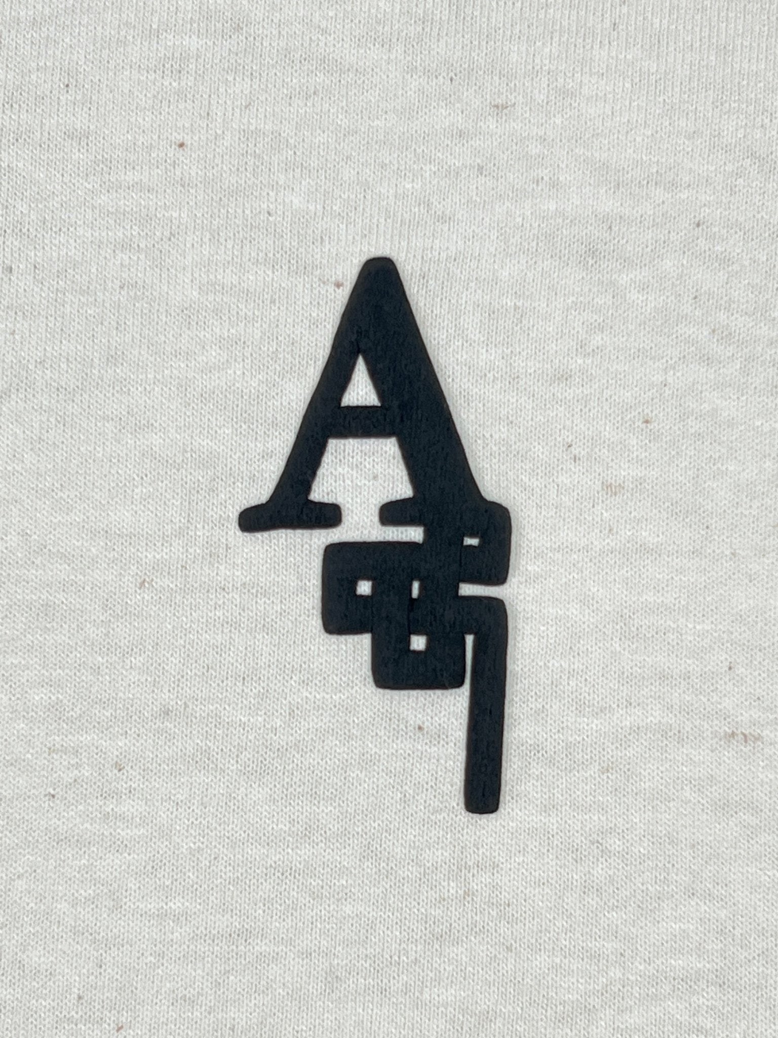 The AL AIN Al Ain AMHX-S821 Makan T-shirt Natural features overlapping black "A" and "S" letters on off-white 100% cotton, made in Italy.
